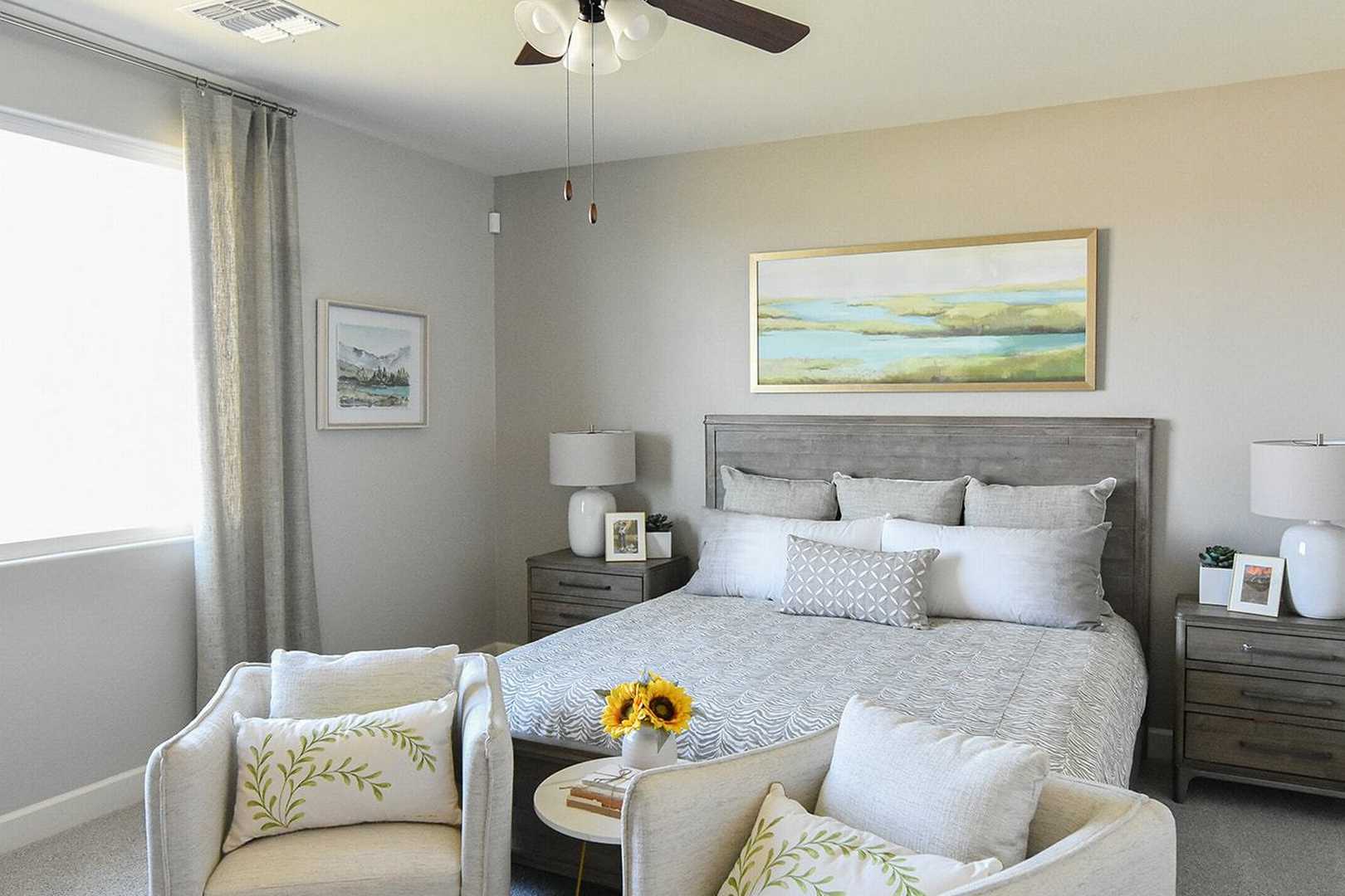 Serene master bedroom in The Summit B featuring king bed with gray headboard, neutral tones, armchairs, and ceiling fan