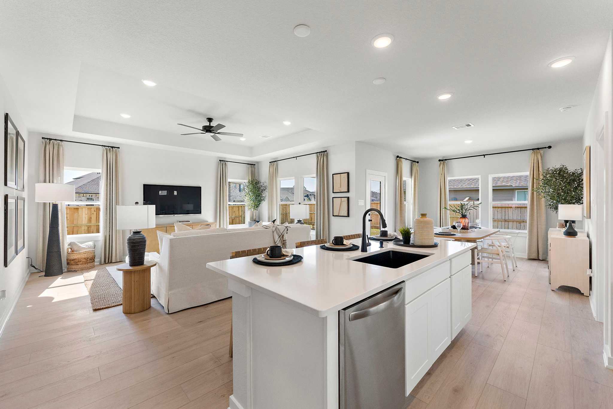 Open-concept kitchen and living room at Sundance Cove in Crosby Texas with white island hardwood floors ceiling fan and large windows