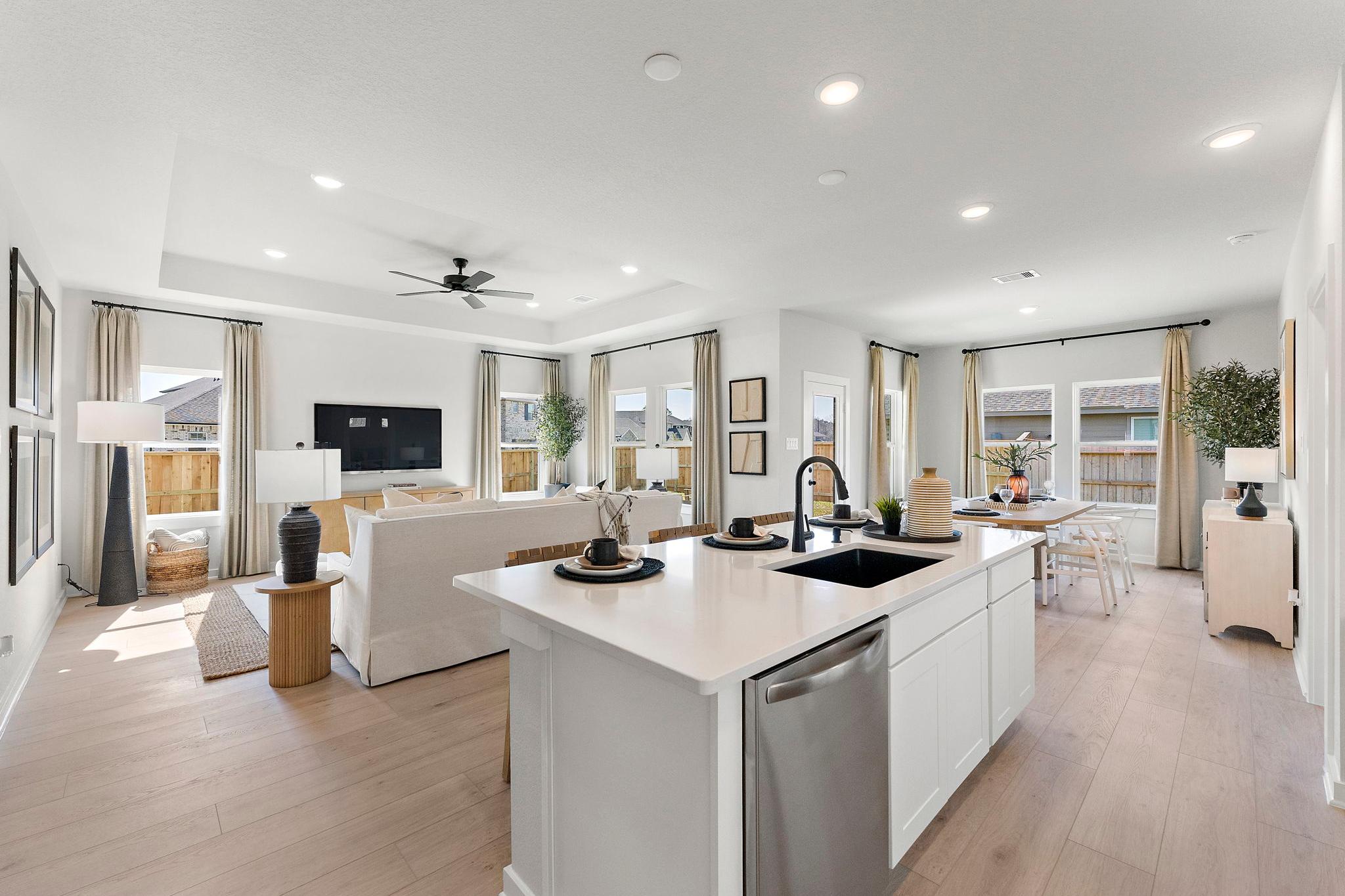 Open-concept kitchen and living room at Sundance Cove in Crosby Texas with white island hardwood floors ceiling fan and large windows