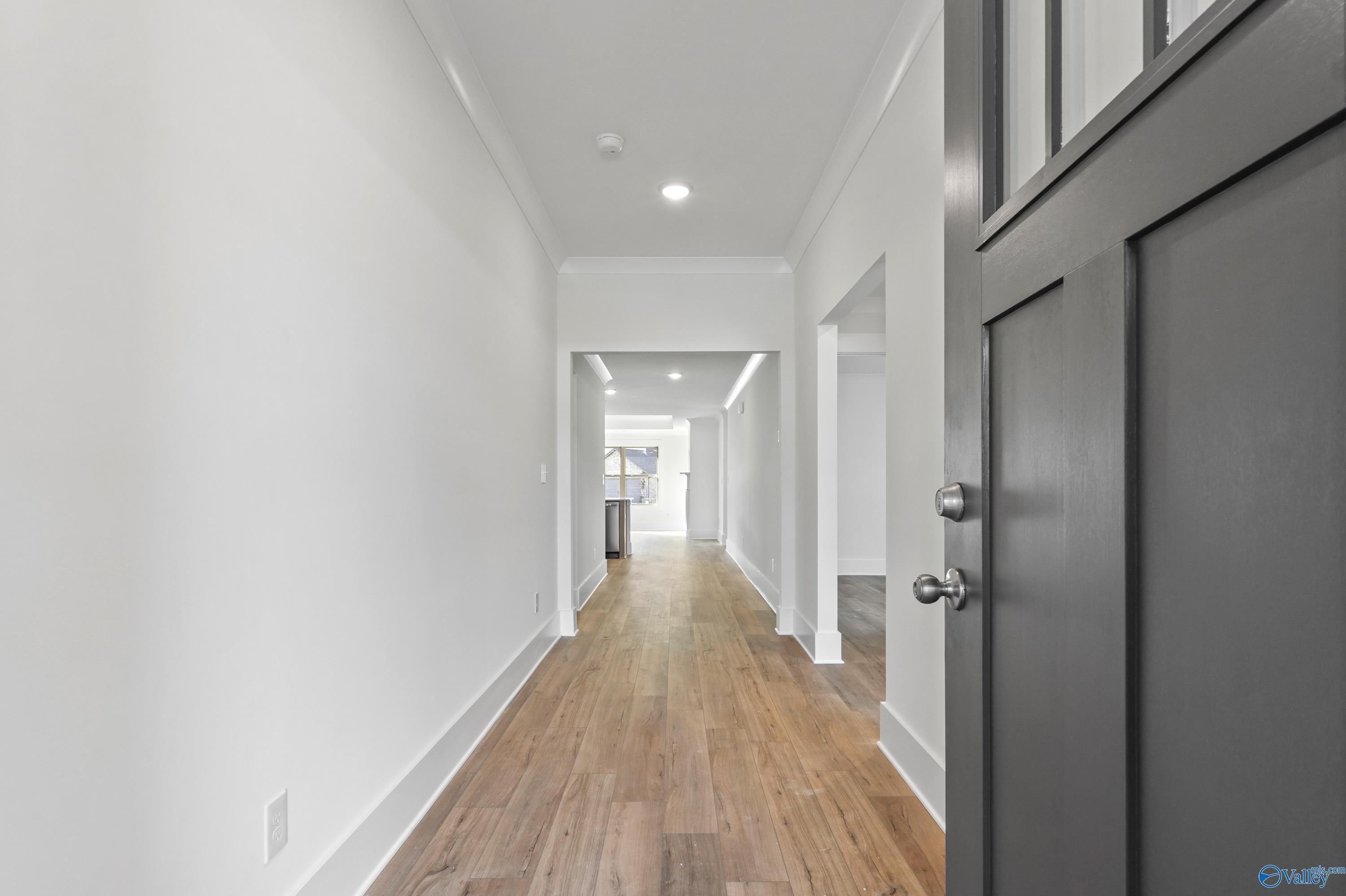 Spacious hallway with hardwood floors, white walls, recessed lights, and black entry door in Davidson Homes The Daphne C, Arab, Alabama