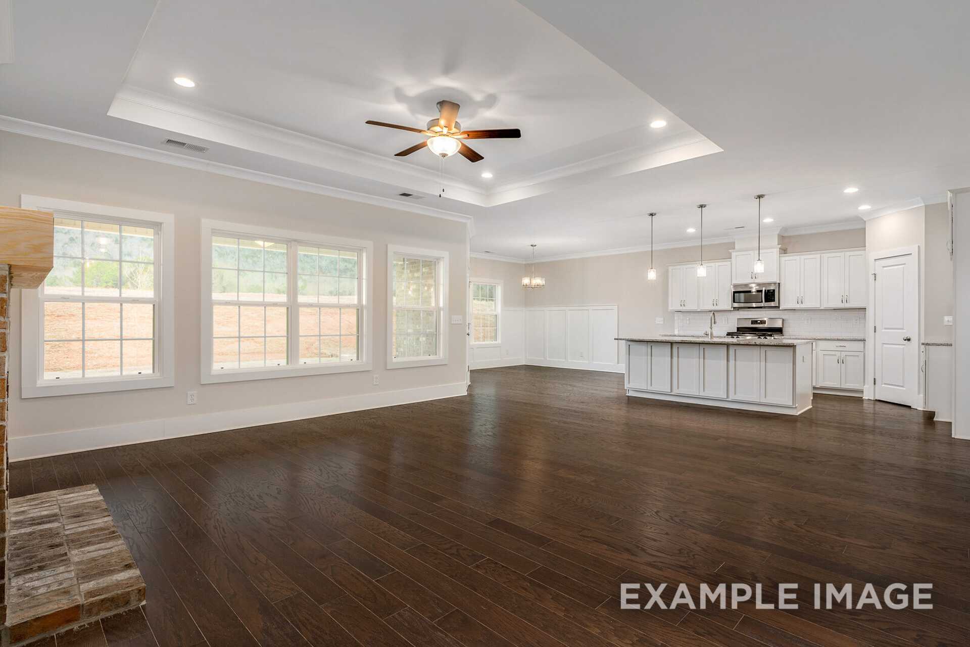 Spacious open-concept kitchen and living area in The Rockford home: hardwood floors, white cabinetry, large island, brick fireplace