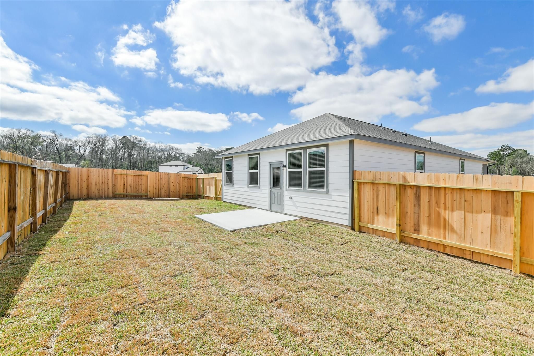 White 1-story The Colorado F home with wooden fenced yard and grassy lawn by Davidson Homes in Liberty Estates, Cleveland, Texas