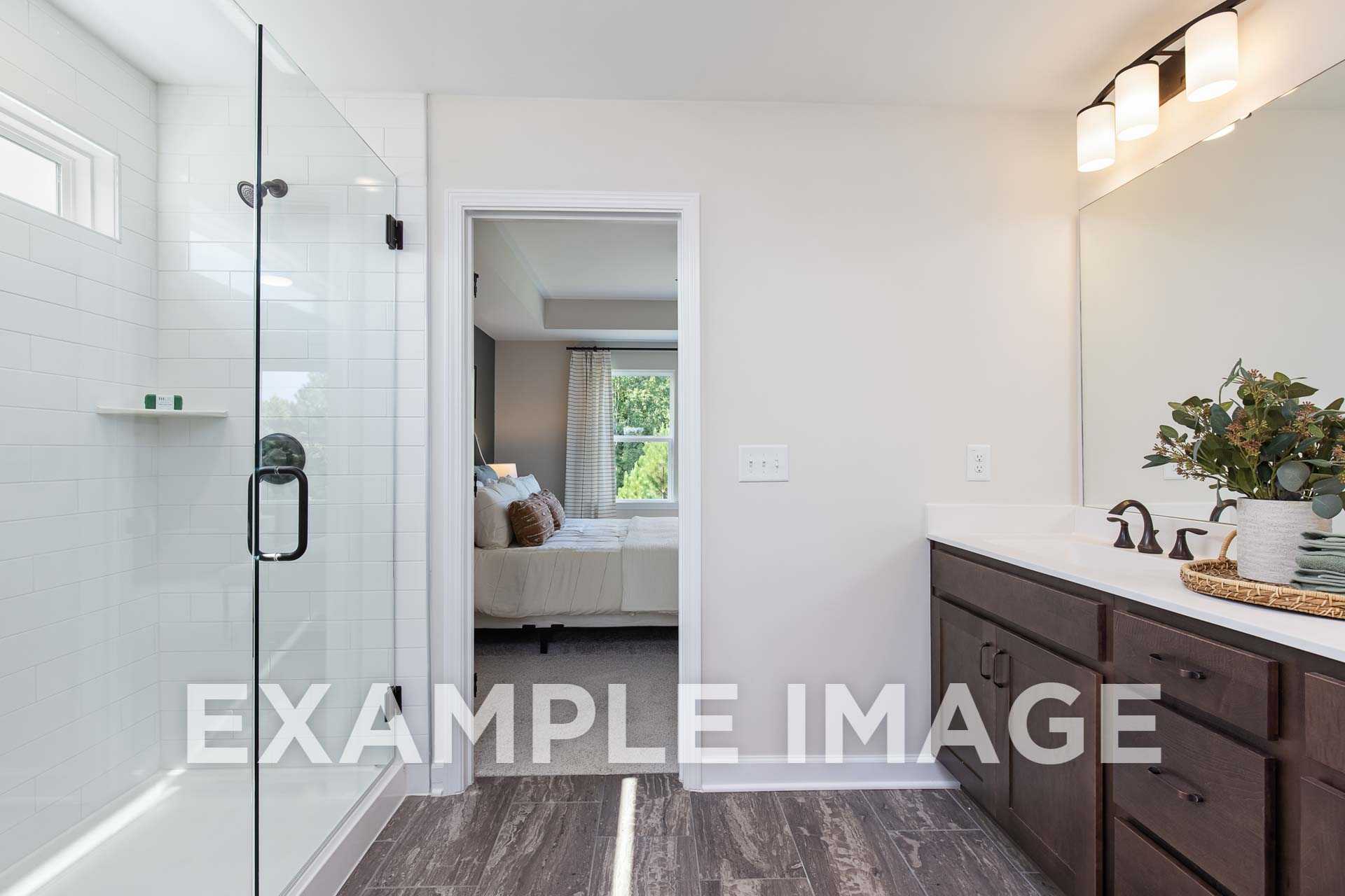 Spacious master bathroom in The Willow F featuring frameless glass shower, double sink vanity, and adjacent bedroom view