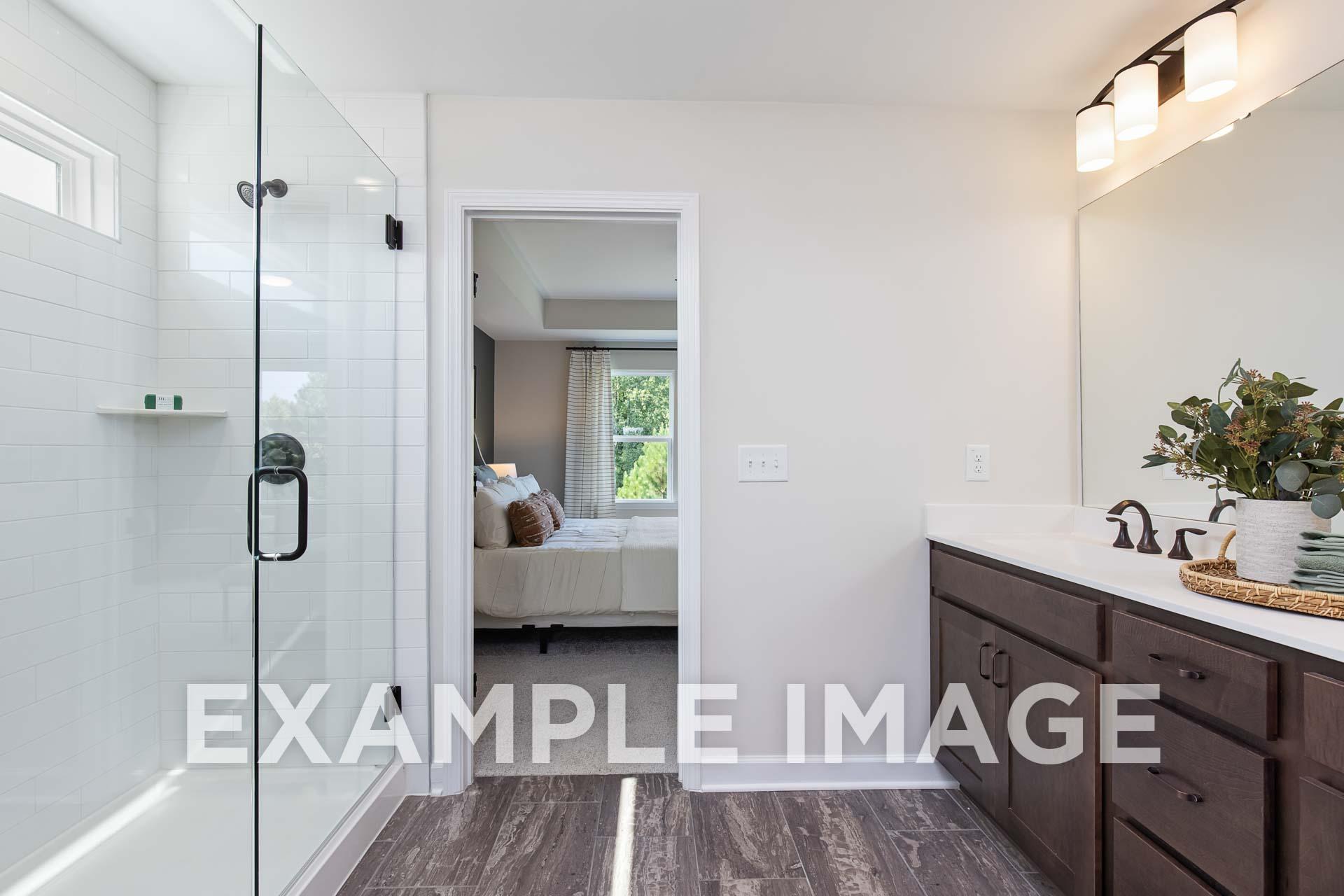 Spacious master bathroom in The Willow E featuring frameless glass shower, double vanity with plants, and adjacent bedroom view