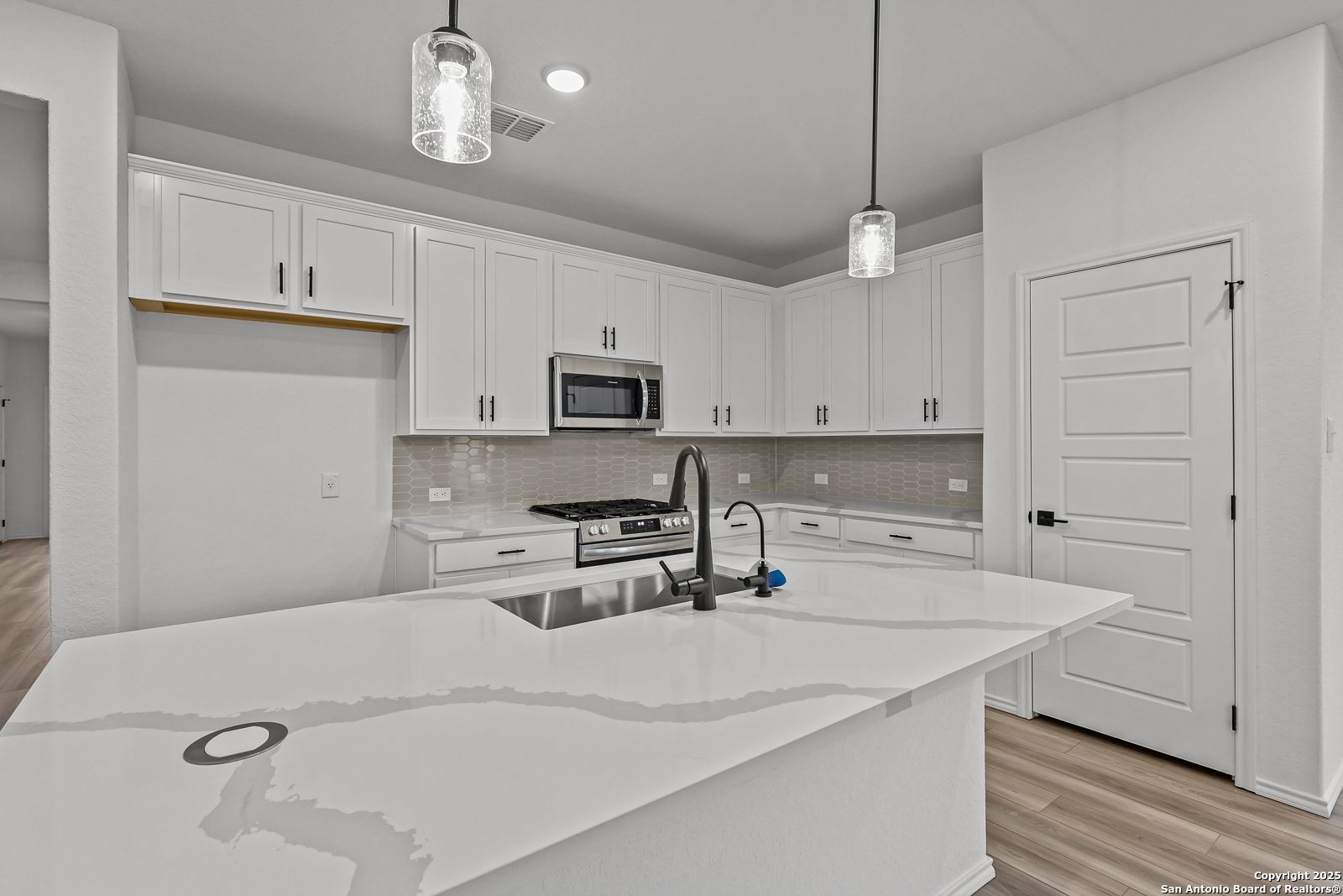 Modern white kitchen with quartz island, stainless appliances, and open layout in The Daphne J by Davidson Homes, Converse TX
