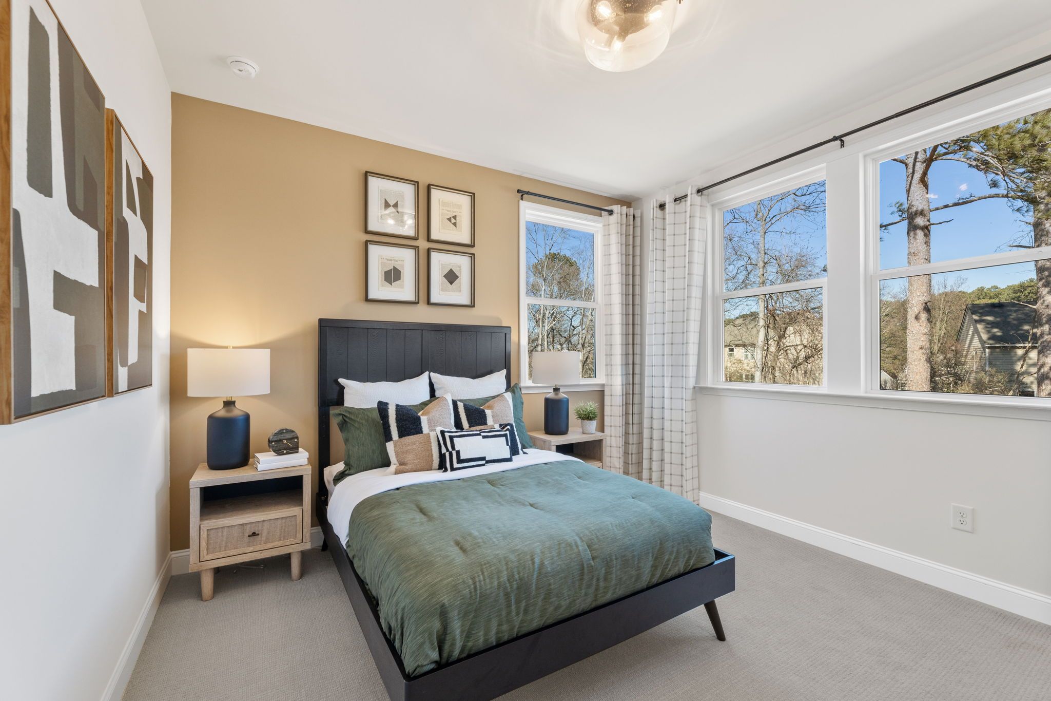 Spacious bedroom interior at Fern Hollow in Buford Georgia featuring black framed bed green bedding large windows and abstract wall art