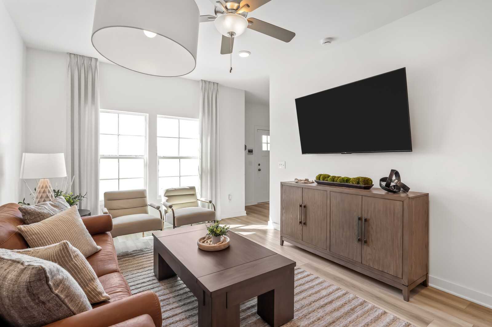 Cozy living room with beige sofa, wooden coffee table, wall TV, and large windows in Davidson Homes The Cumberland B, Gallatin, TN
