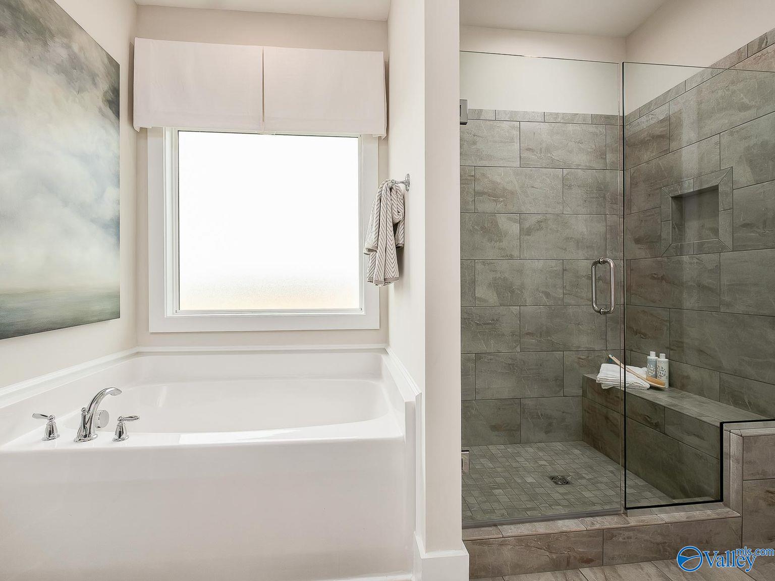Elegant master bathroom featuring freestanding tub, tiled walk-in shower with bench, and large window in Davidson Homes The Everett, Toney, Alabama