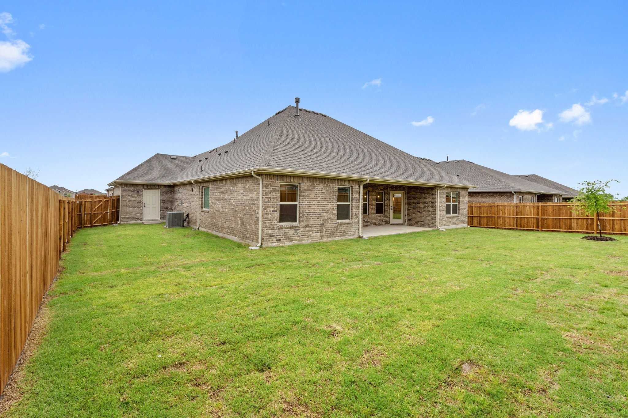 Back view of The Rockford C 4-bedroom home featuring covered patio, brick exterior, and fenced grassy backyard in Waverly Estates, Josephine, Texas