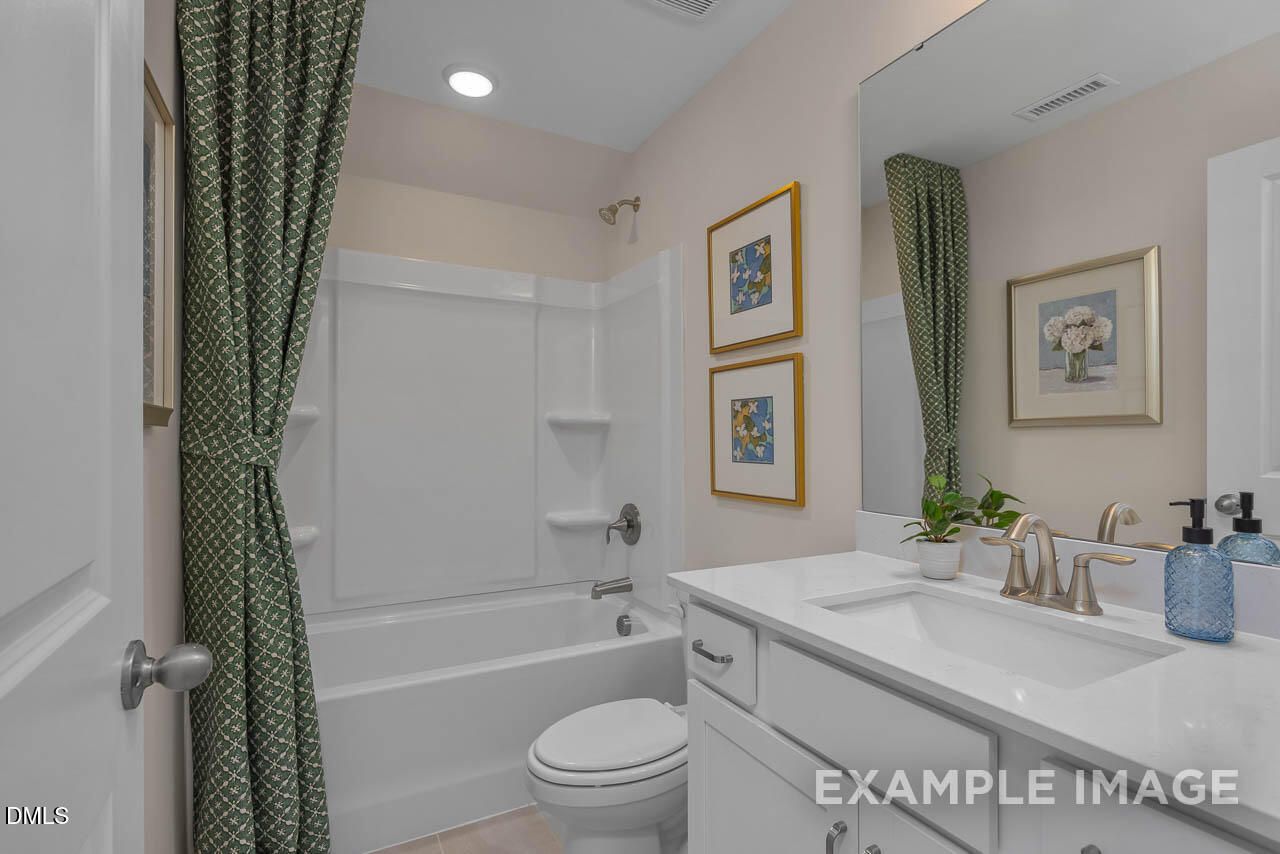 Modern bathroom with white tub, green patterned curtains, vanity sink, mirror, and framed art in Davidson Homes Hickory II C, Wake Forest, NC