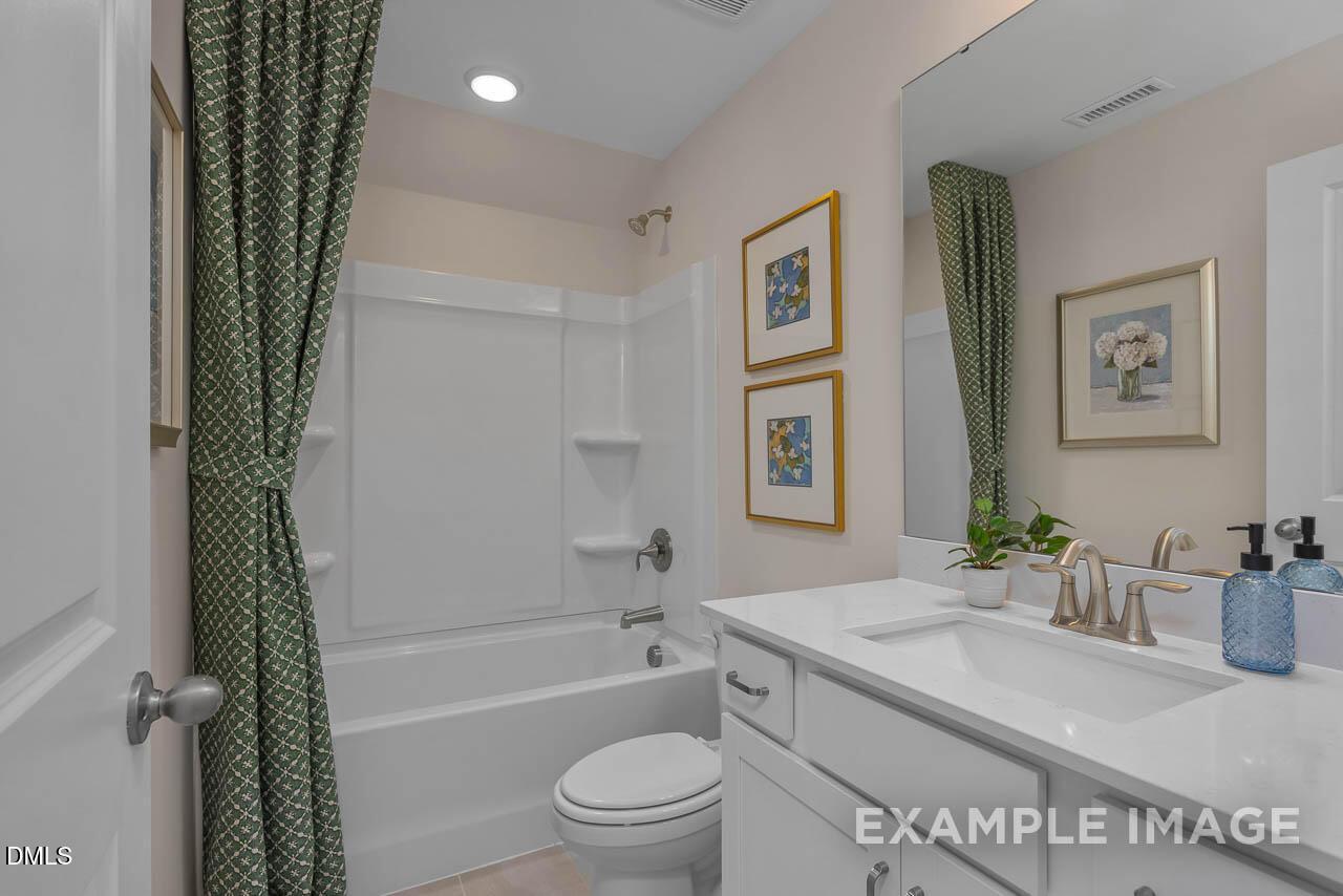 Modern bathroom with white tub, green patterned curtains, vanity sink, mirror, and framed art in Davidson Homes Hickory II C, Wake Forest, NC