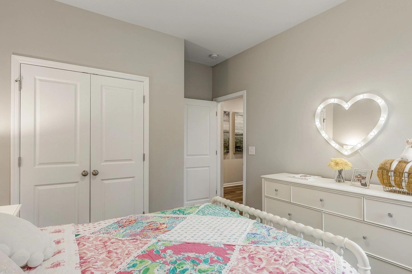 Charming girl's bedroom at Carroll Green in Harvest Alabama with colorful quilt bed white dresser neon heart mirror
