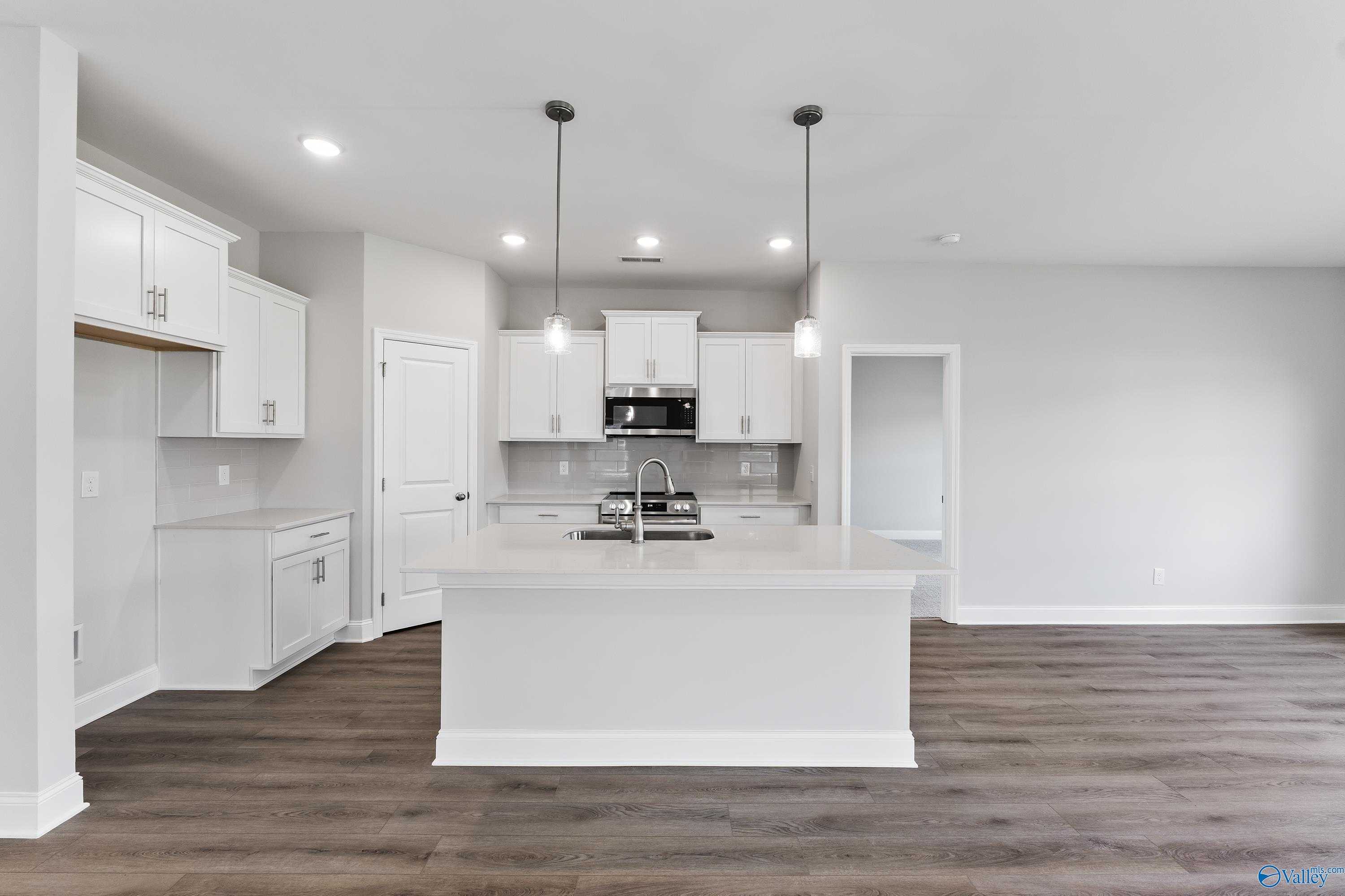 Modern white kitchen with large island sink, stainless appliances, and pendant lights in Davidson Homes Franklin C, Toney, Alabama
