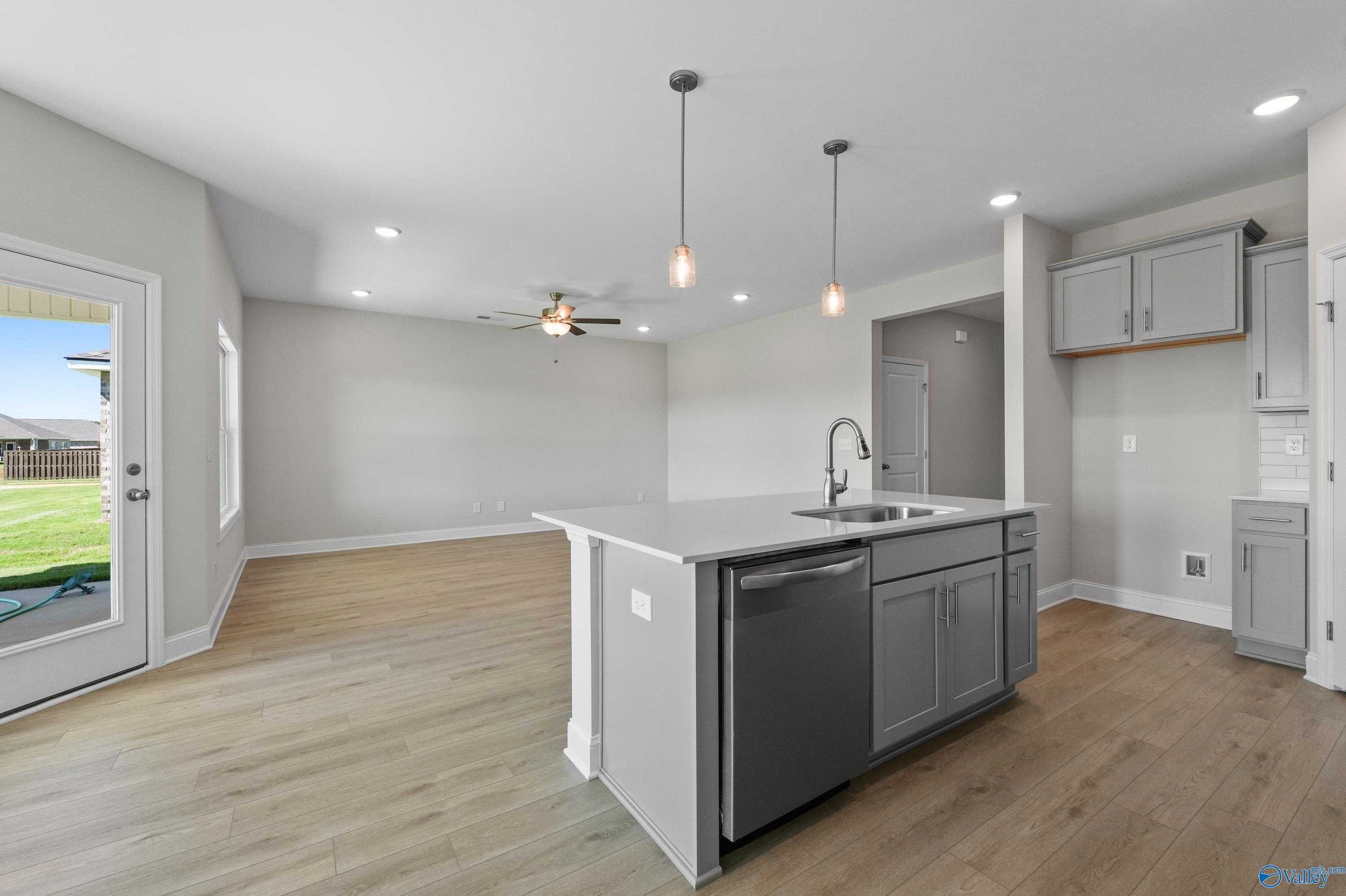 Modern open-concept kitchen with gray island sink, dishwasher, and sliding doors to backyard in Davidson Homes The Everett, Hazel Green, AL