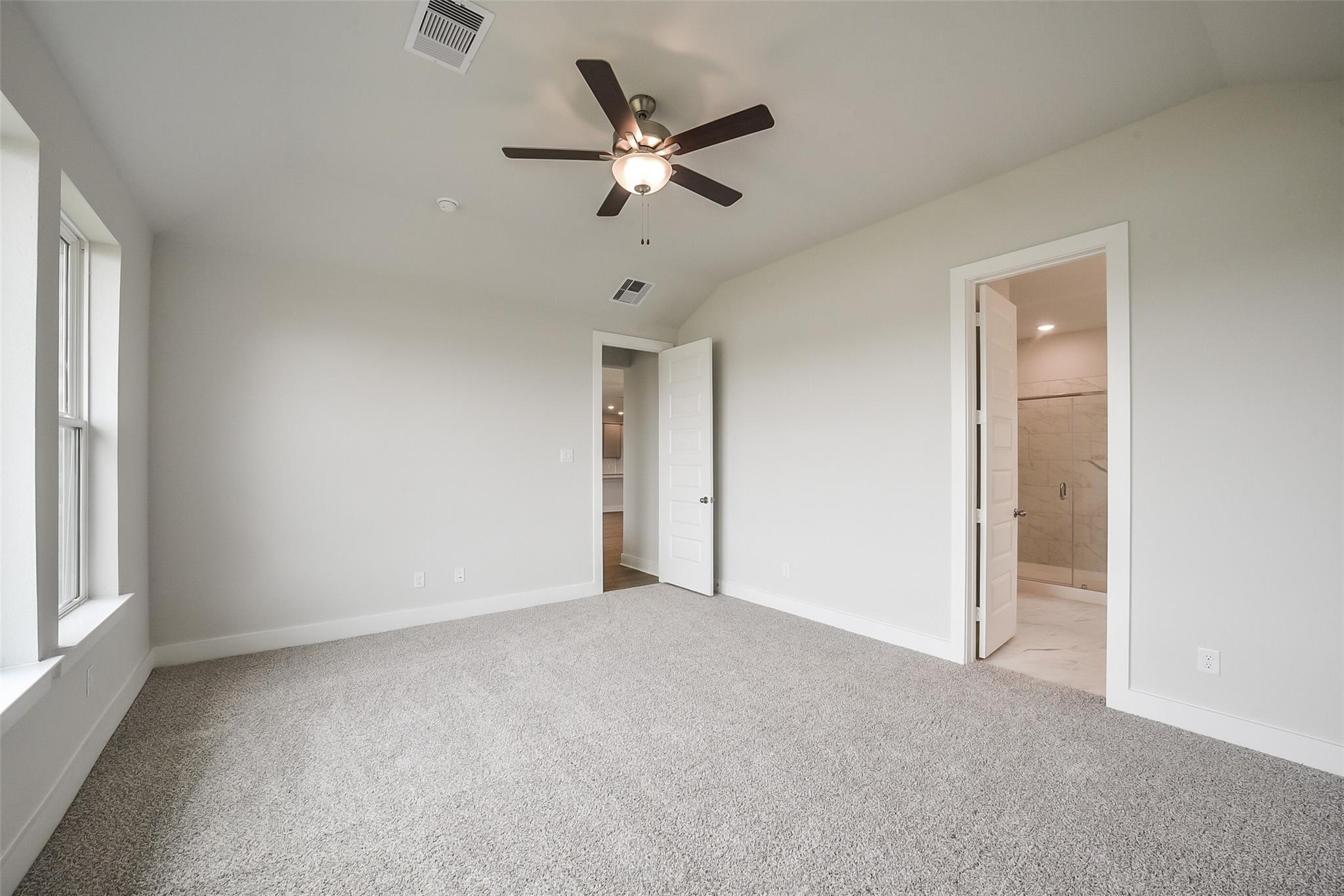Spacious master bedroom with ceiling fan, en-suite bath, beige walls, and large windows in Davidson Homes The Philip B, Rosharon, Texas
