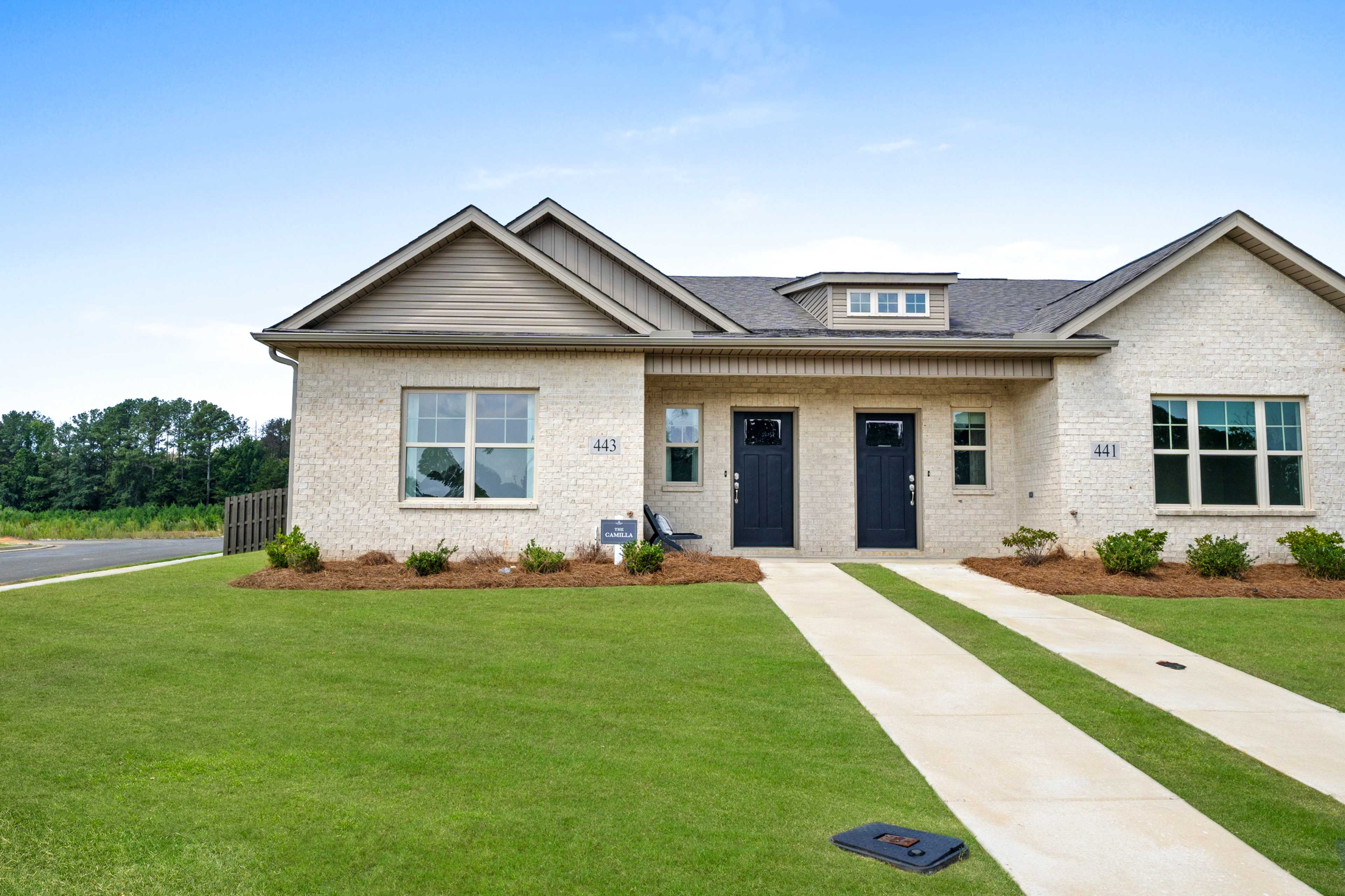 Beige brick duplex townhome exterior at The Retreat at Cain Park in Hartselle AL with dual entry doors, walkway, and lush landscaping