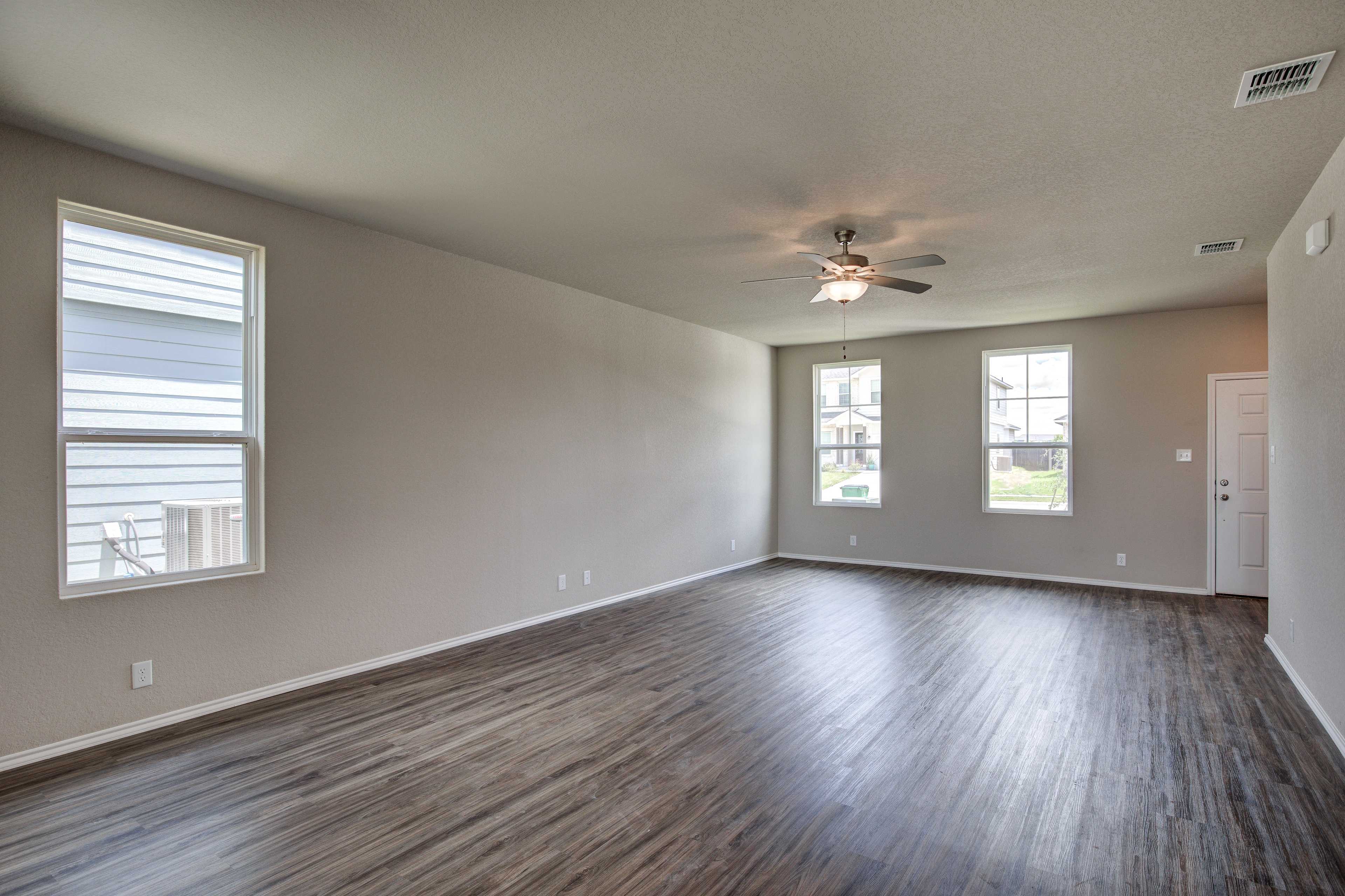 Spacious living room in The Murray Davidson Homes design featuring beige walls, large windows, ceiling fan, and dark hardwood floors