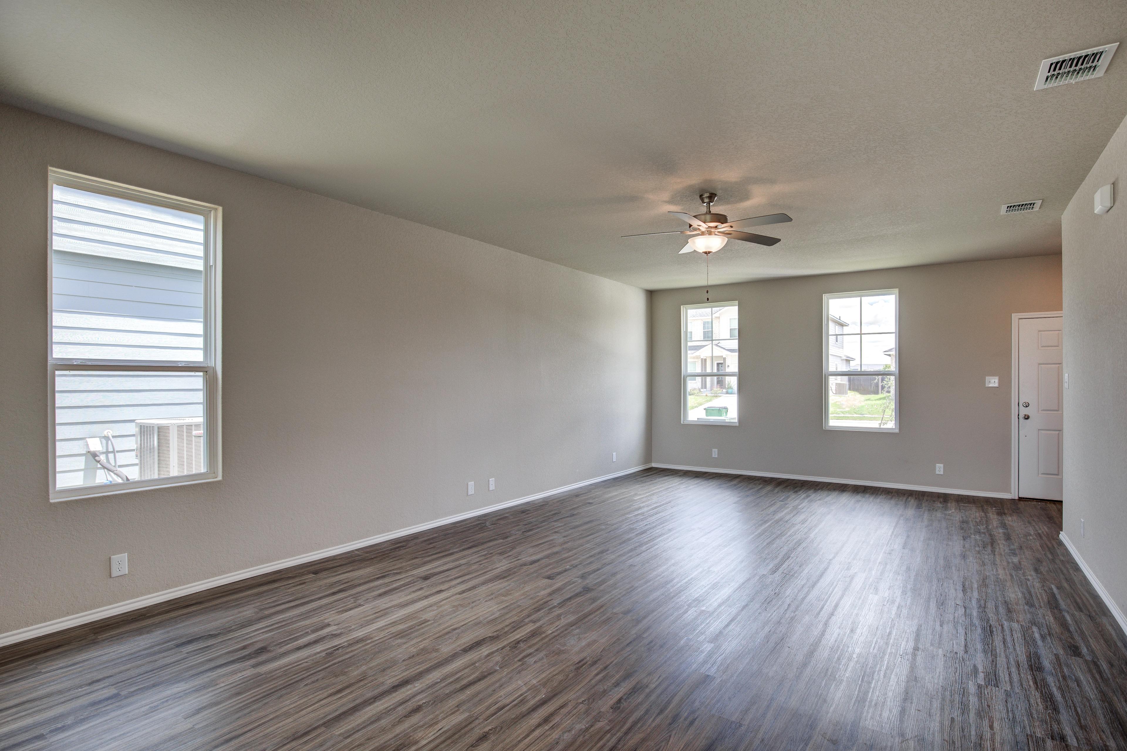 Spacious open-concept living room in The Murray G home with hardwood floors, beige walls, large windows, and ceiling fan