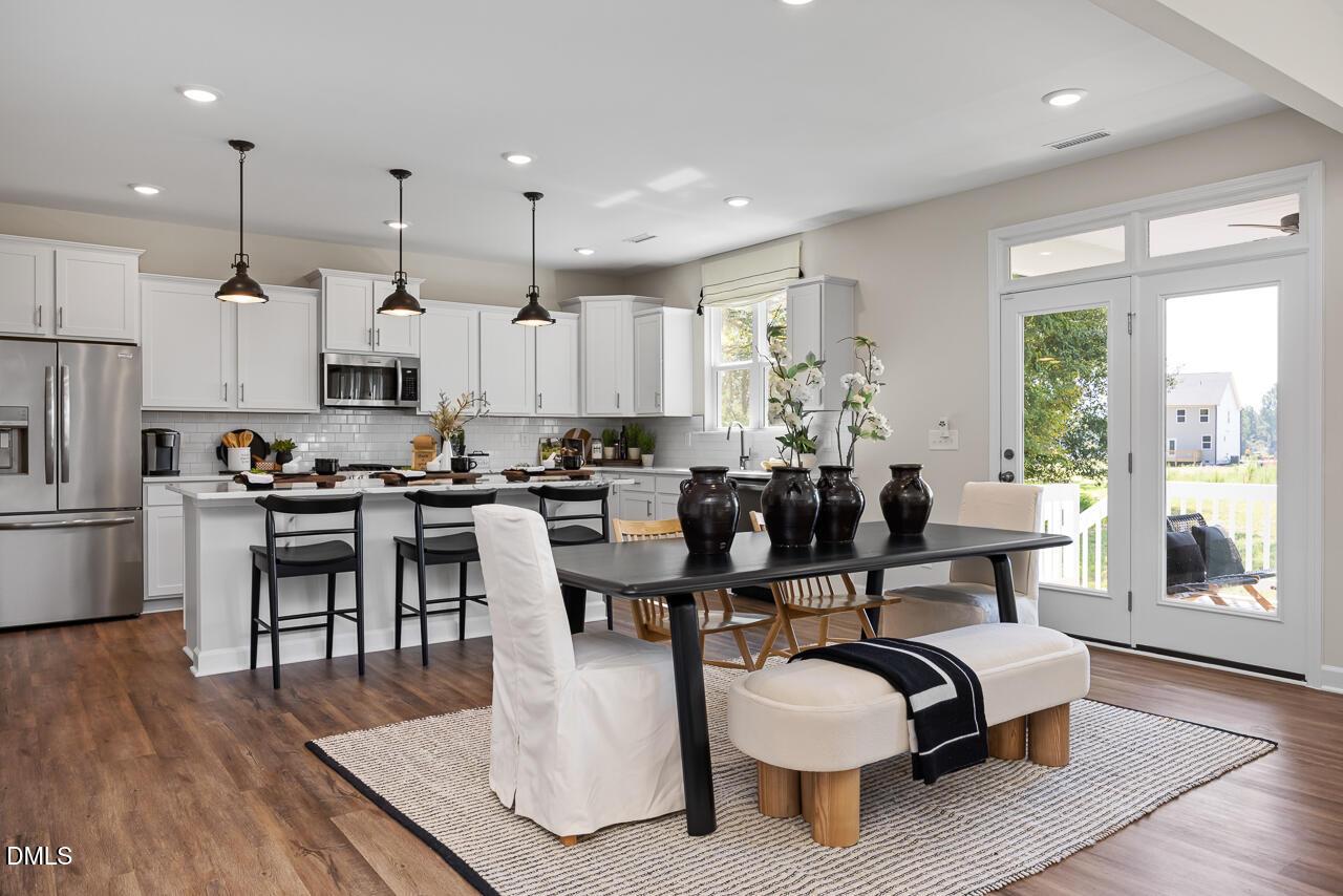 Modern open kitchen with white cabinets, stainless fridge, black dining table, and French doors to backyard in The Hickory II B, Zebulon, NC