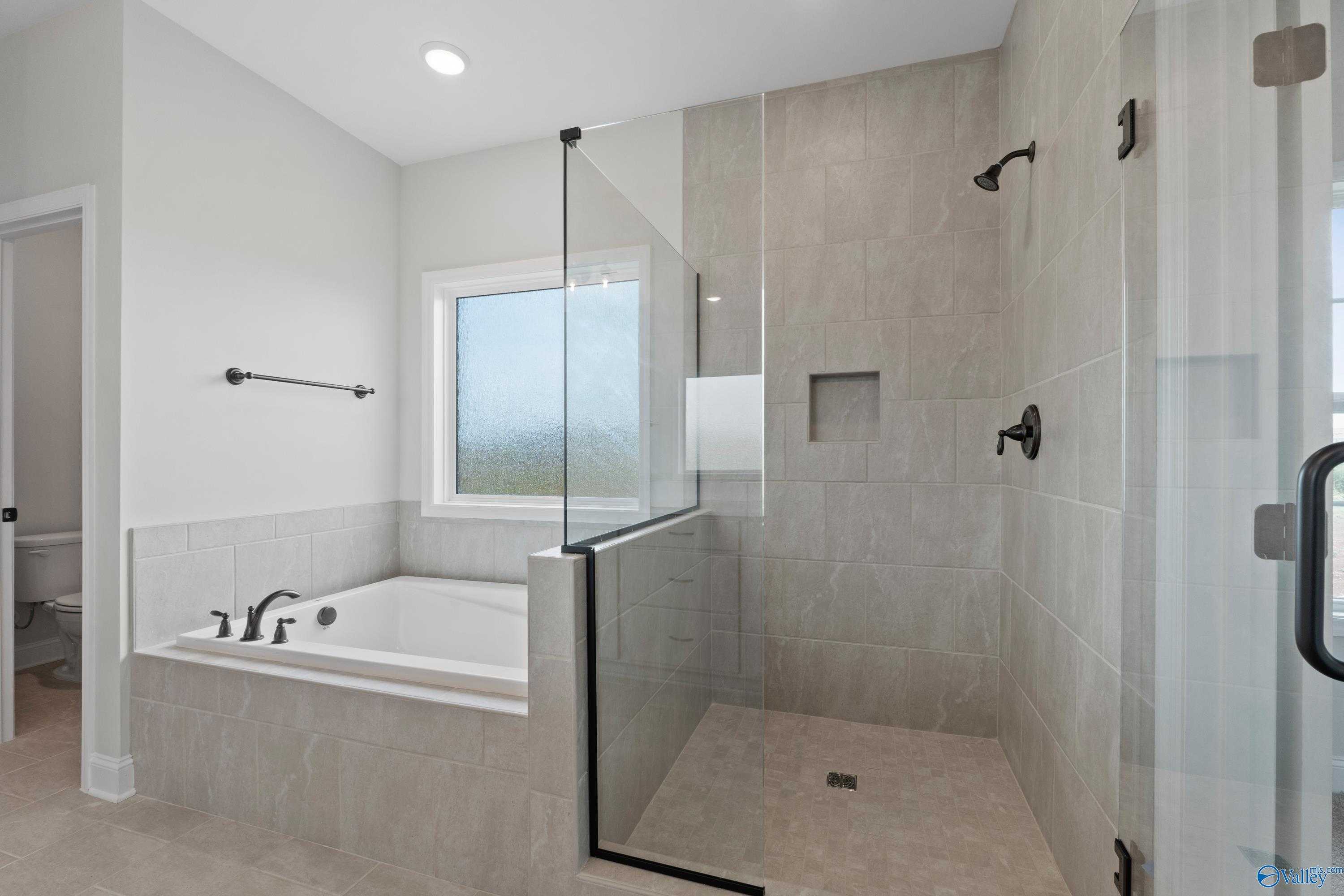 Modern master bathroom with frameless glass shower, soaking tub, and tile accents in Davidson Homes The Kirkland with Bonus, Harvest, Alabama