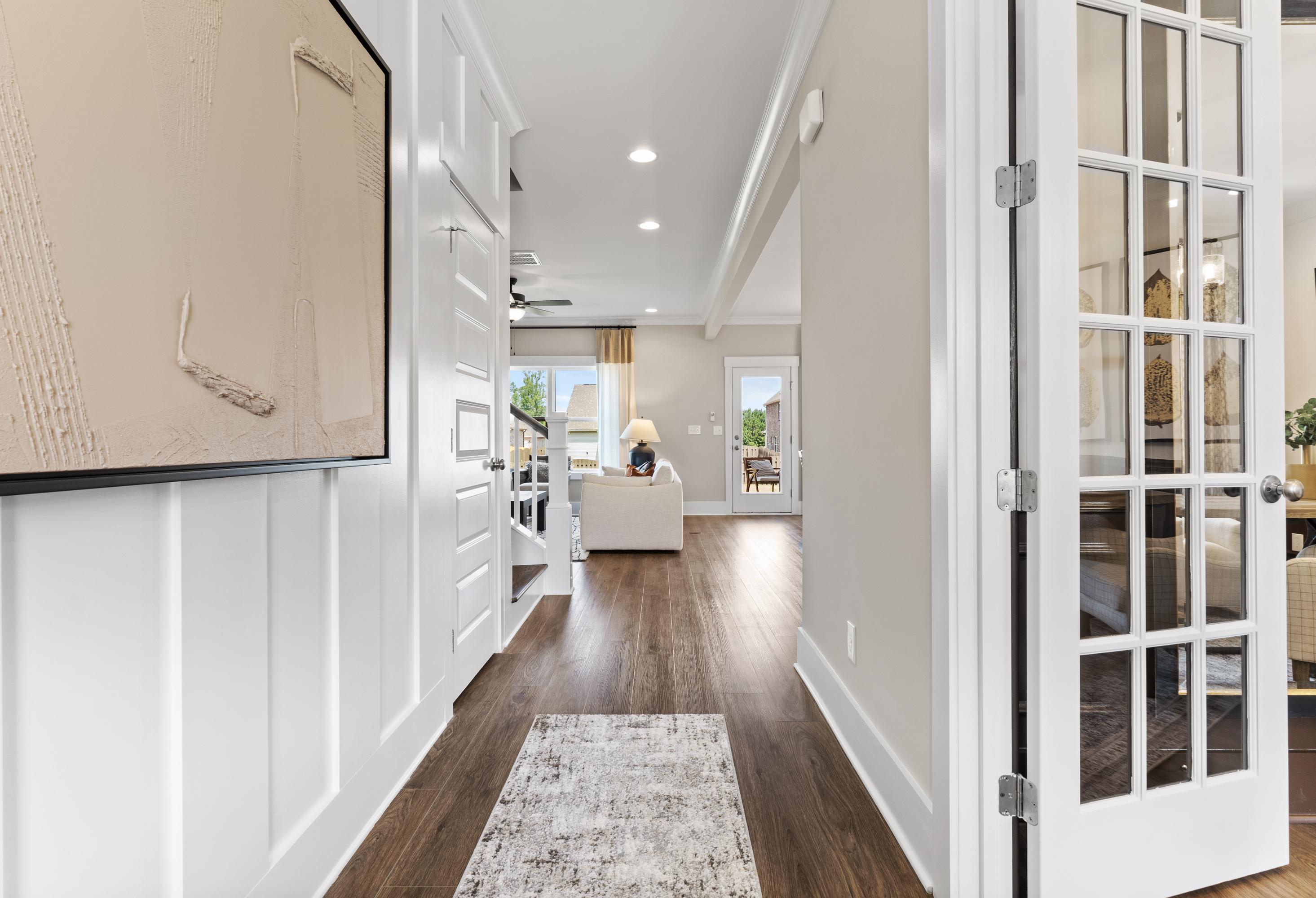 Spacious entryway hallway in The Shelby A home with white wainscoting, hardwood floors, French doors to cozy living area