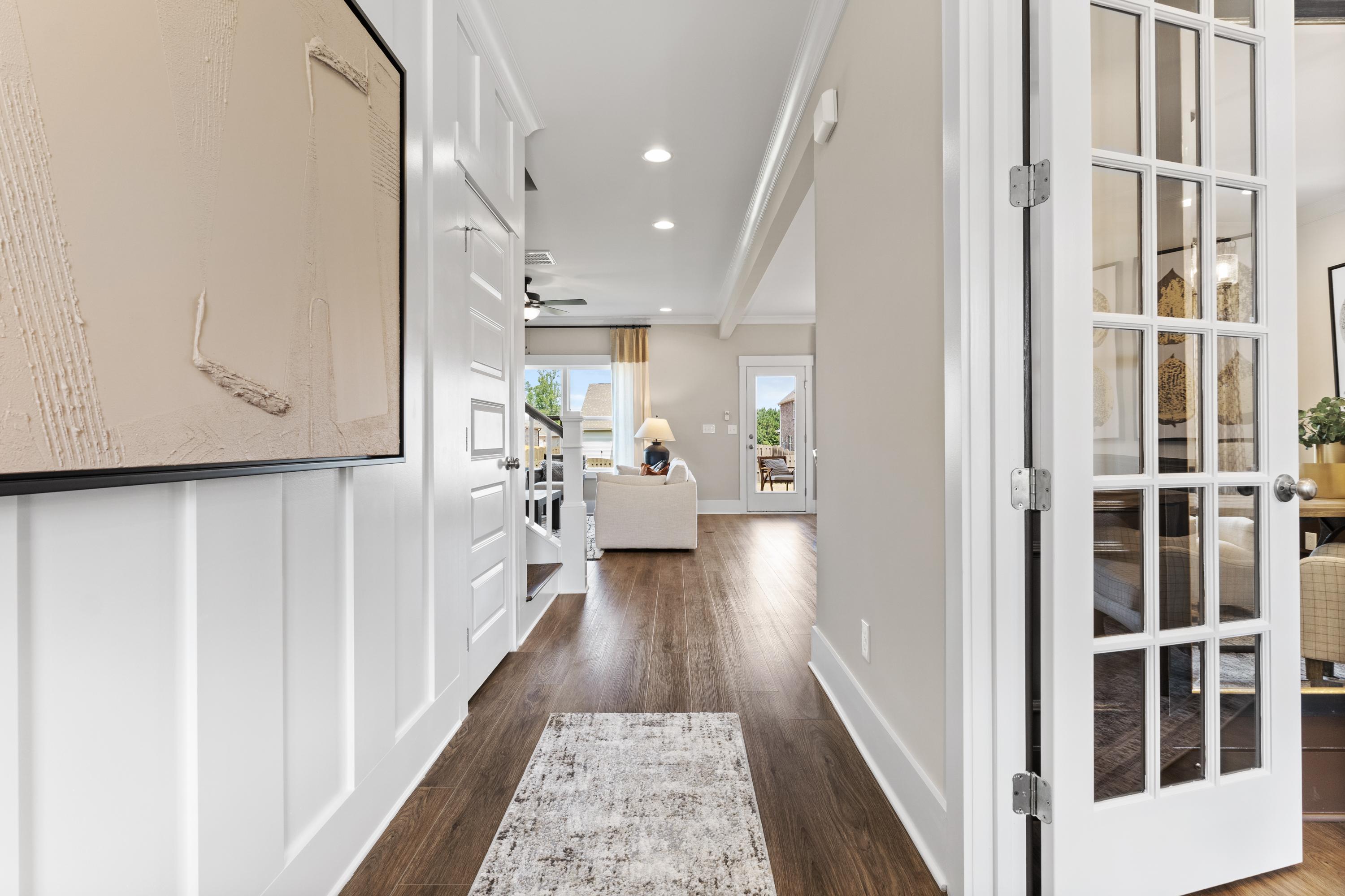 Spacious entryway hallway in The Shelby A home with white wainscoting, hardwood floors, French doors to cozy living area