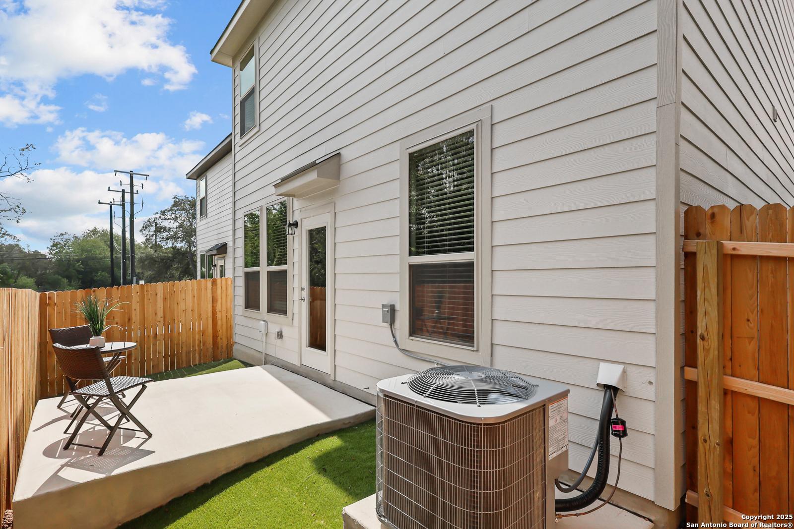 Back view of two-story The Gillian C home by Davidson Homes with covered patio, wooden fence, AC unit, and green lawn in Cedar Heights, San Antonio, Texas