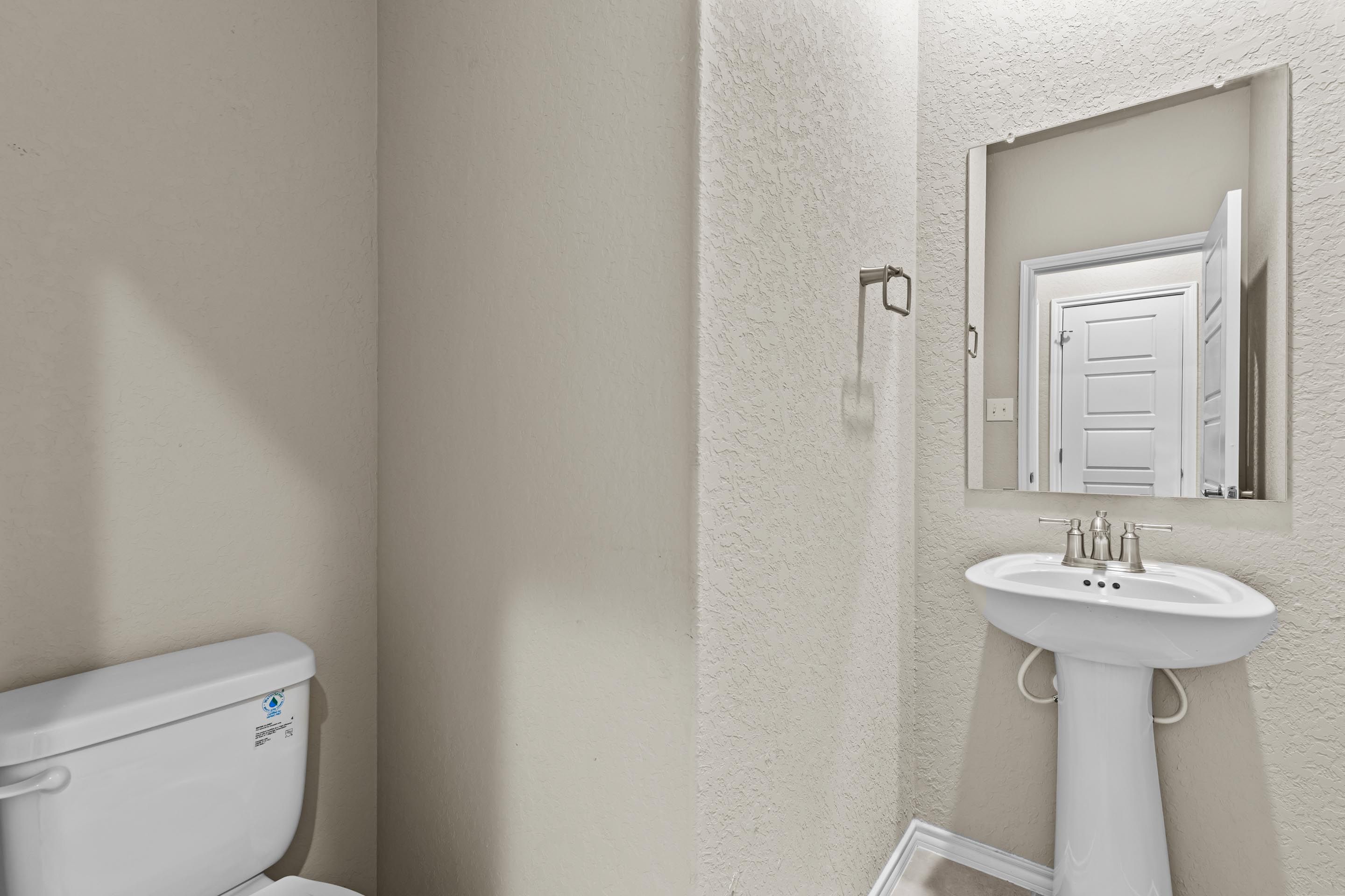 Modern powder room featuring pedestal sink, toilet, and framed mirror in Davidson Homes The Douglas F, Royal Crest, San Antonio