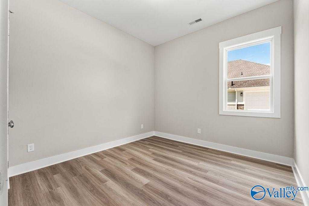 Bright empty bedroom with light gray walls, luxury vinyl plank flooring, and large window in Evermore Homes The Oxford, Owens Cross Roads, AL