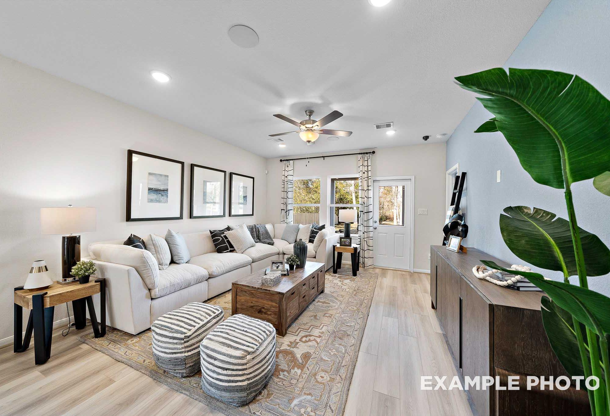 Spacious living room in The San Marcos home featuring white L-shaped sofa, wooden tables, ceiling fan, and lush potted plant