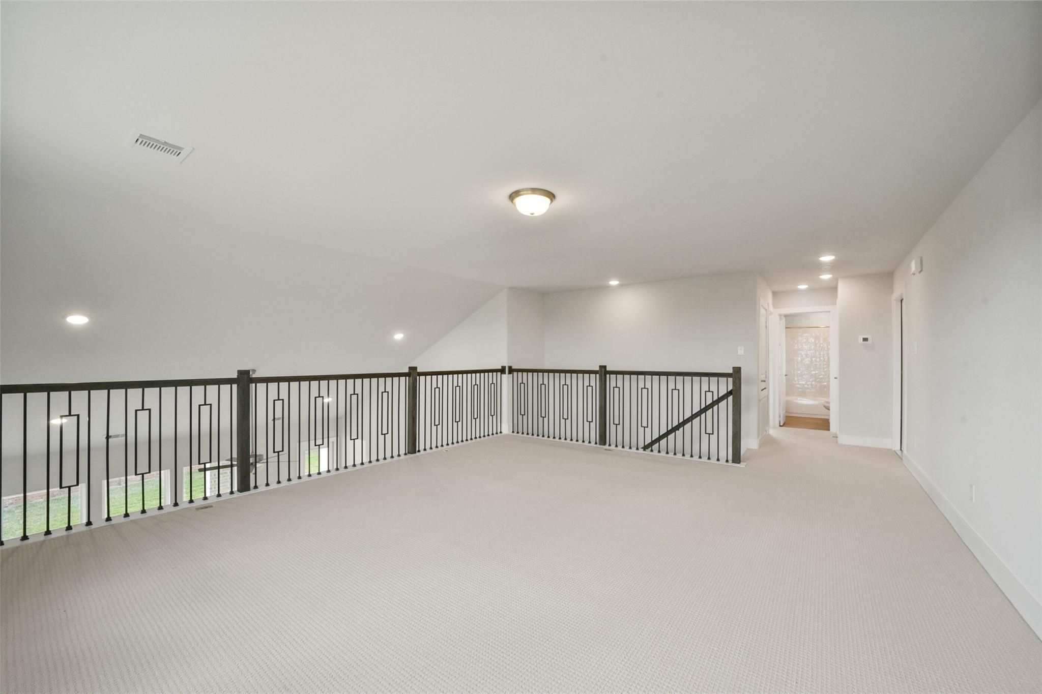 Spacious upstairs loft with black metal railing, beige carpet, and recessed lights in Davidson Homes The Zion A, Lago Mar, Texas City