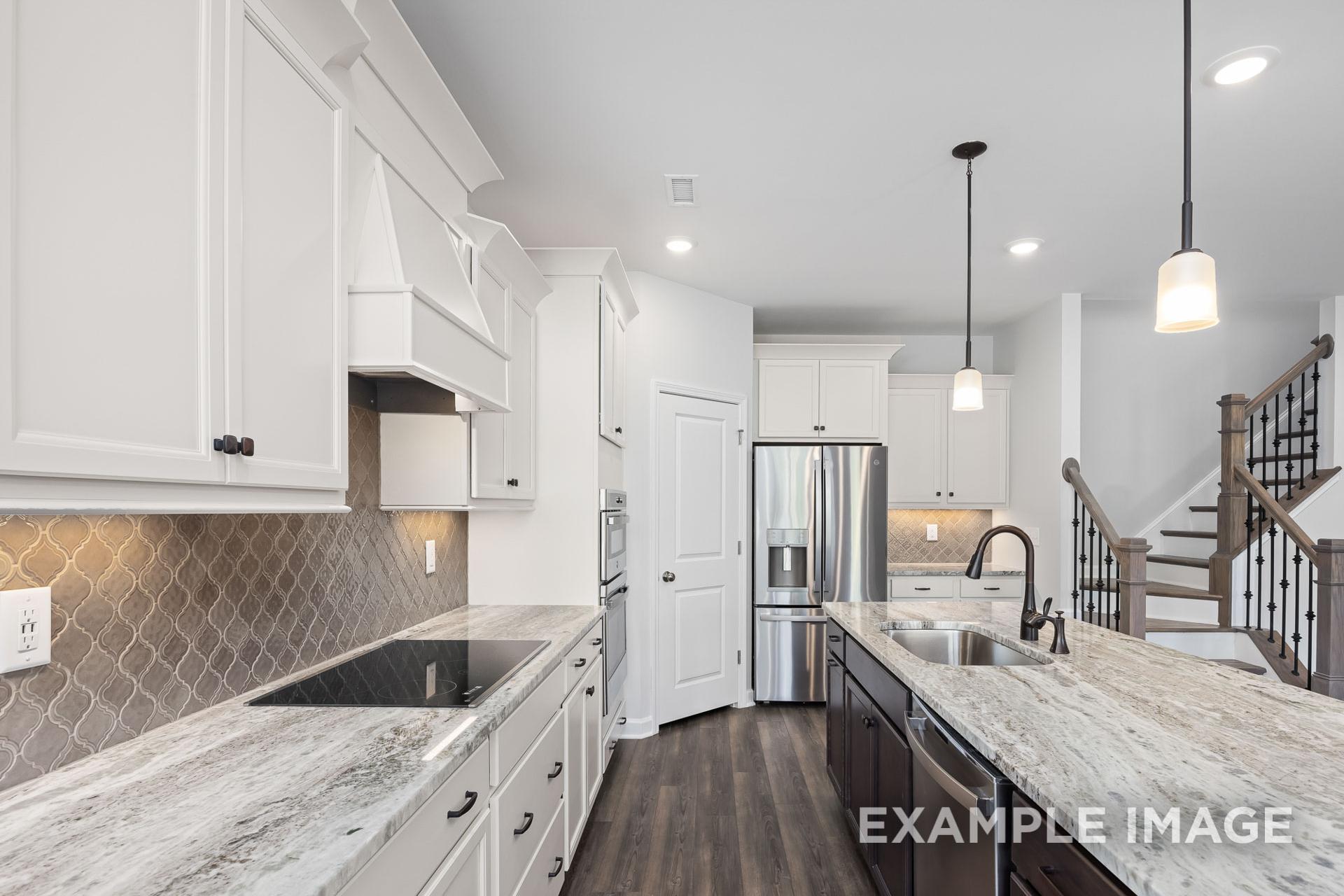 Spacious kitchen in The Grace C with white shaker cabinets, gray quartz island, stainless appliances, and open staircase