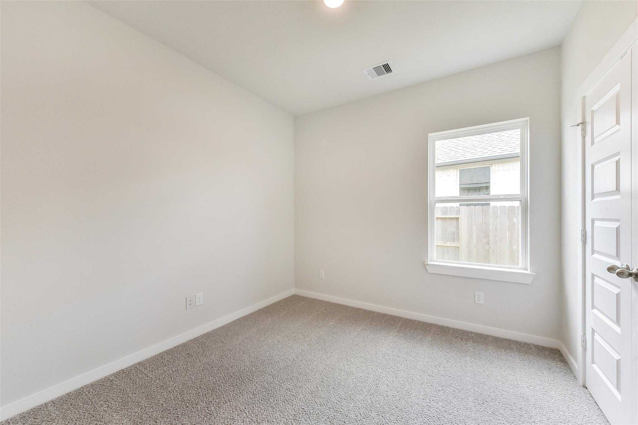 Empty secondary bedroom with neutral beige walls, gray carpet, large window, and white doors in Davidson Homes The Laguna C, Rosharon, Texas
