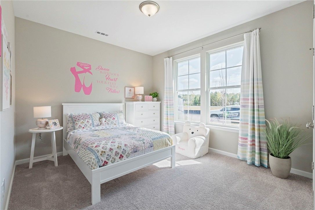 Cozy girl's bedroom featuring ballet wall decal, white bed with patchwork quilt, dresser, and natural light in Davidson Homes The Phoenix B, Opelika