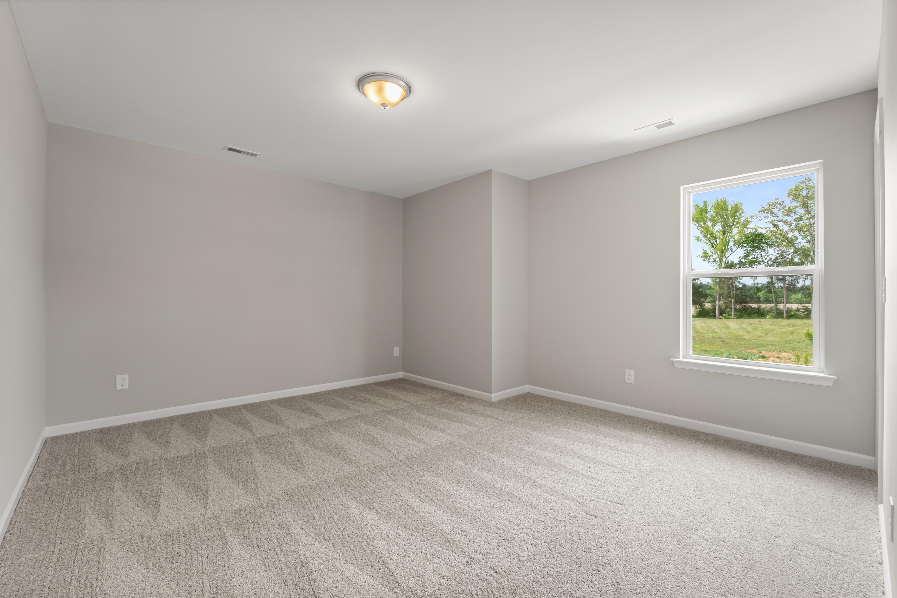 Bright empty bedroom in The Haven E home design with gray walls, carpeted floor, and window view of green fields