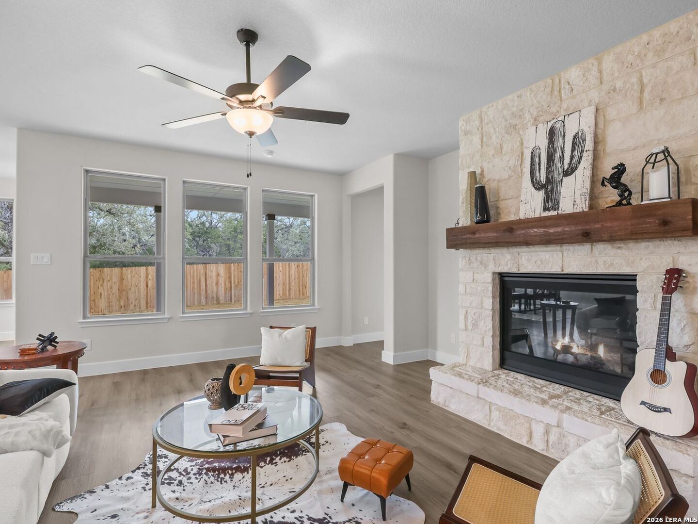 Living room with stone fireplace and wood mantle in The Belmont H floor plan at Potranco Oaks, Castroville, Texas.