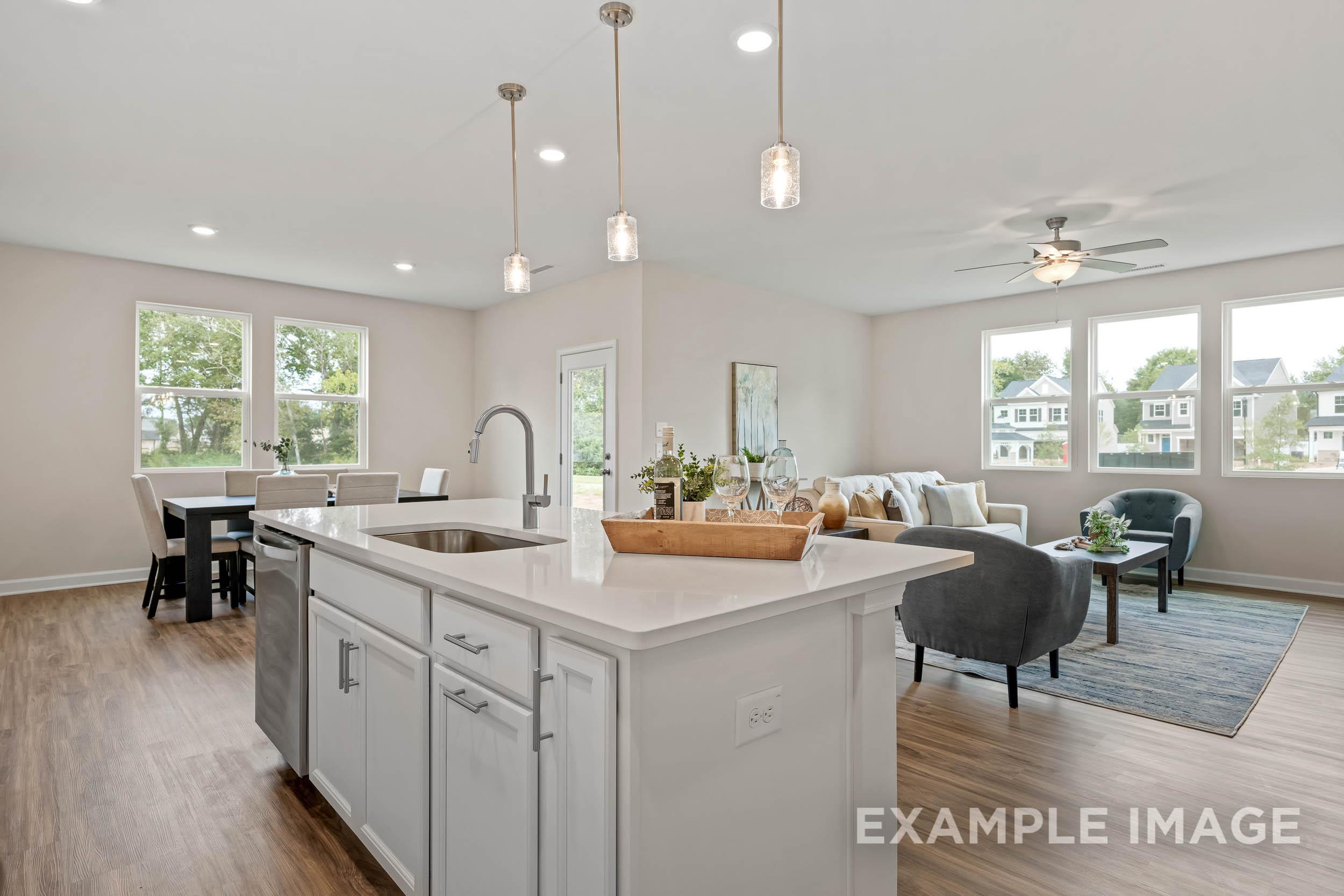Spacious open-concept kitchen and living area in The Preston B with white island sink, dining table, and gray sofa