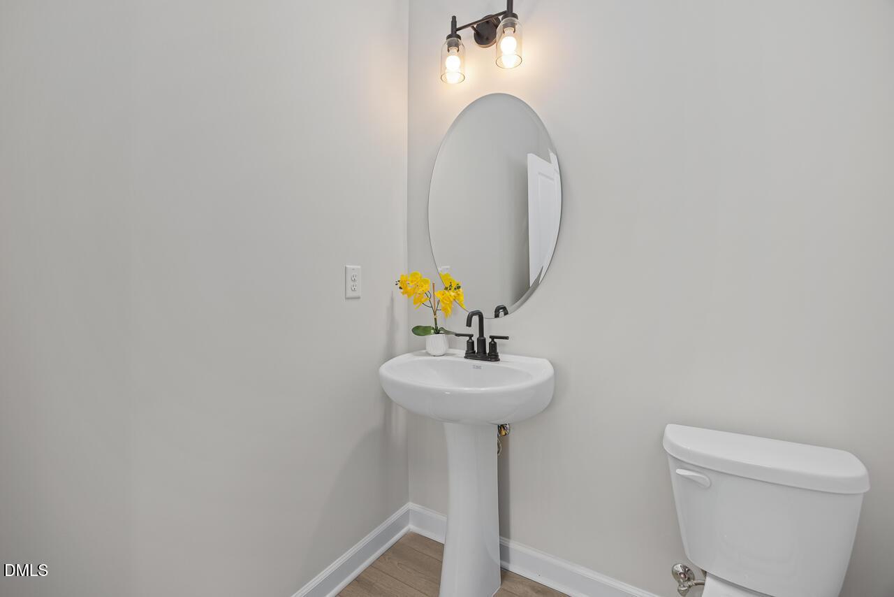 Modern powder room with pedestal sink, oval mirror, and chic lighting in The Ash C floor plan at Woodland Crossing.