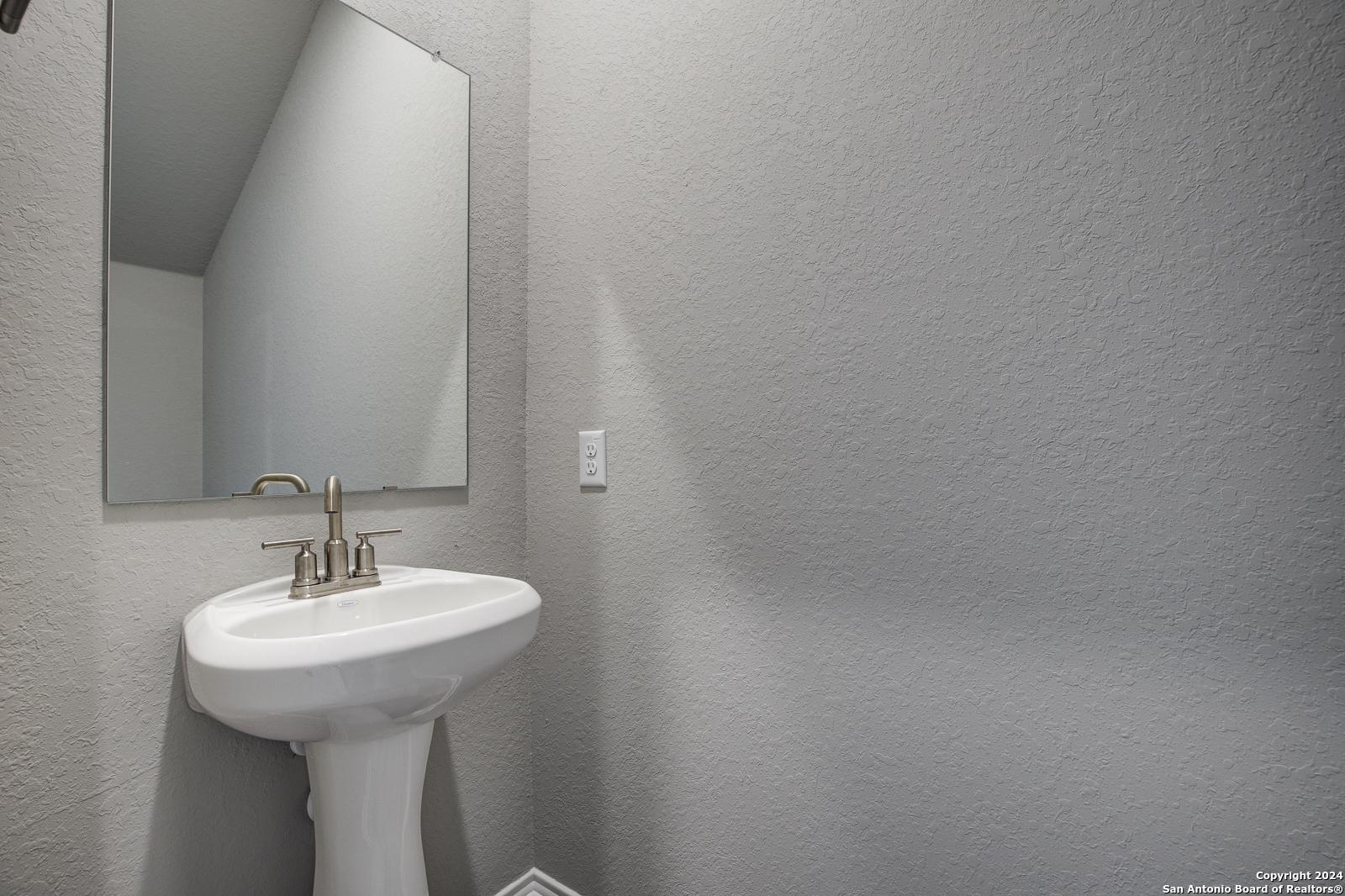 Modern powder room with white pedestal sink, bronze faucet, and frameless mirror in Davidson Homes The Blanco C, San Antonio