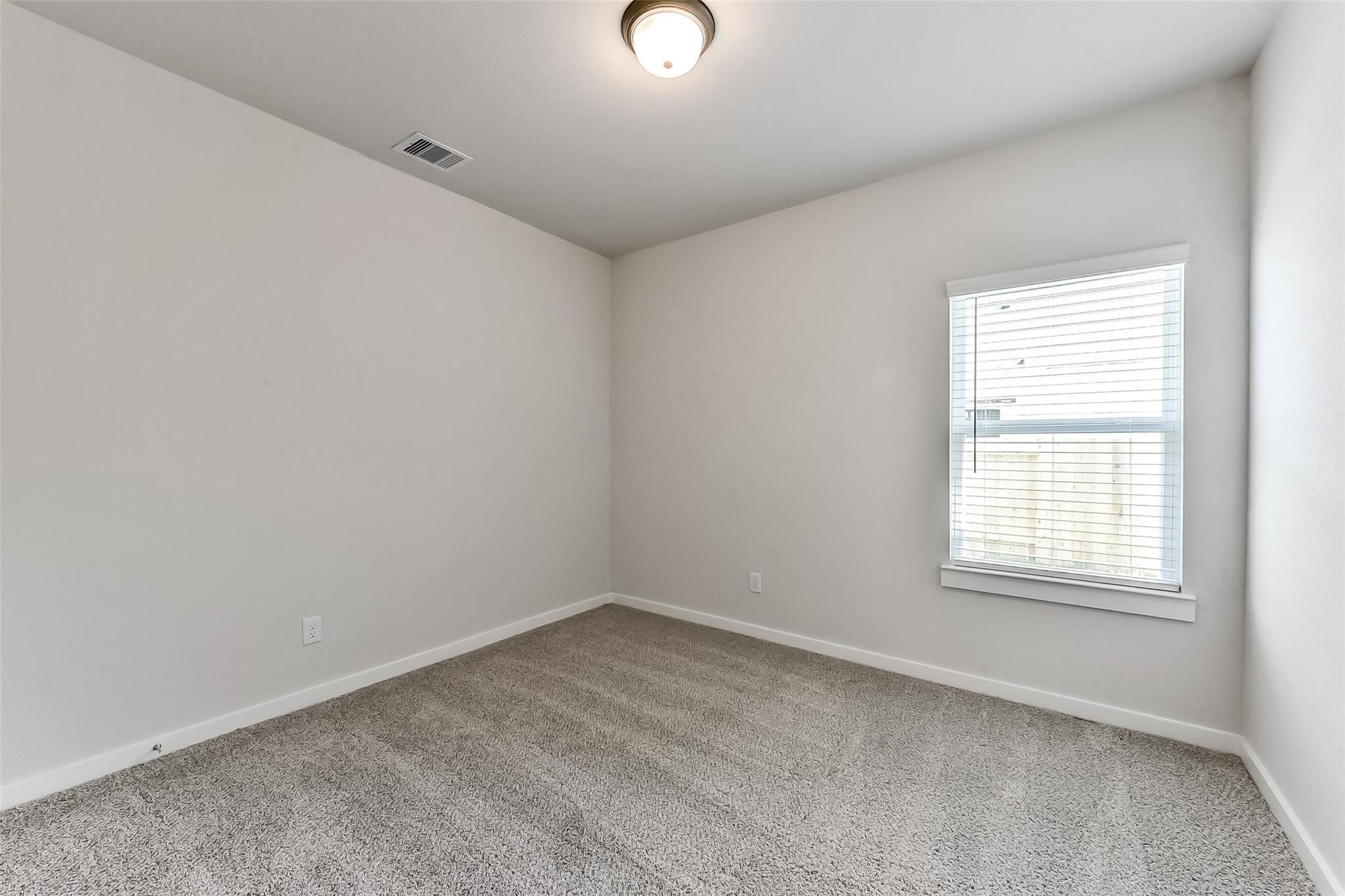 Spacious empty bedroom with neutral walls, beige carpet, and large window blinds in Davidson Homes The Costa B, Dayton, Texas