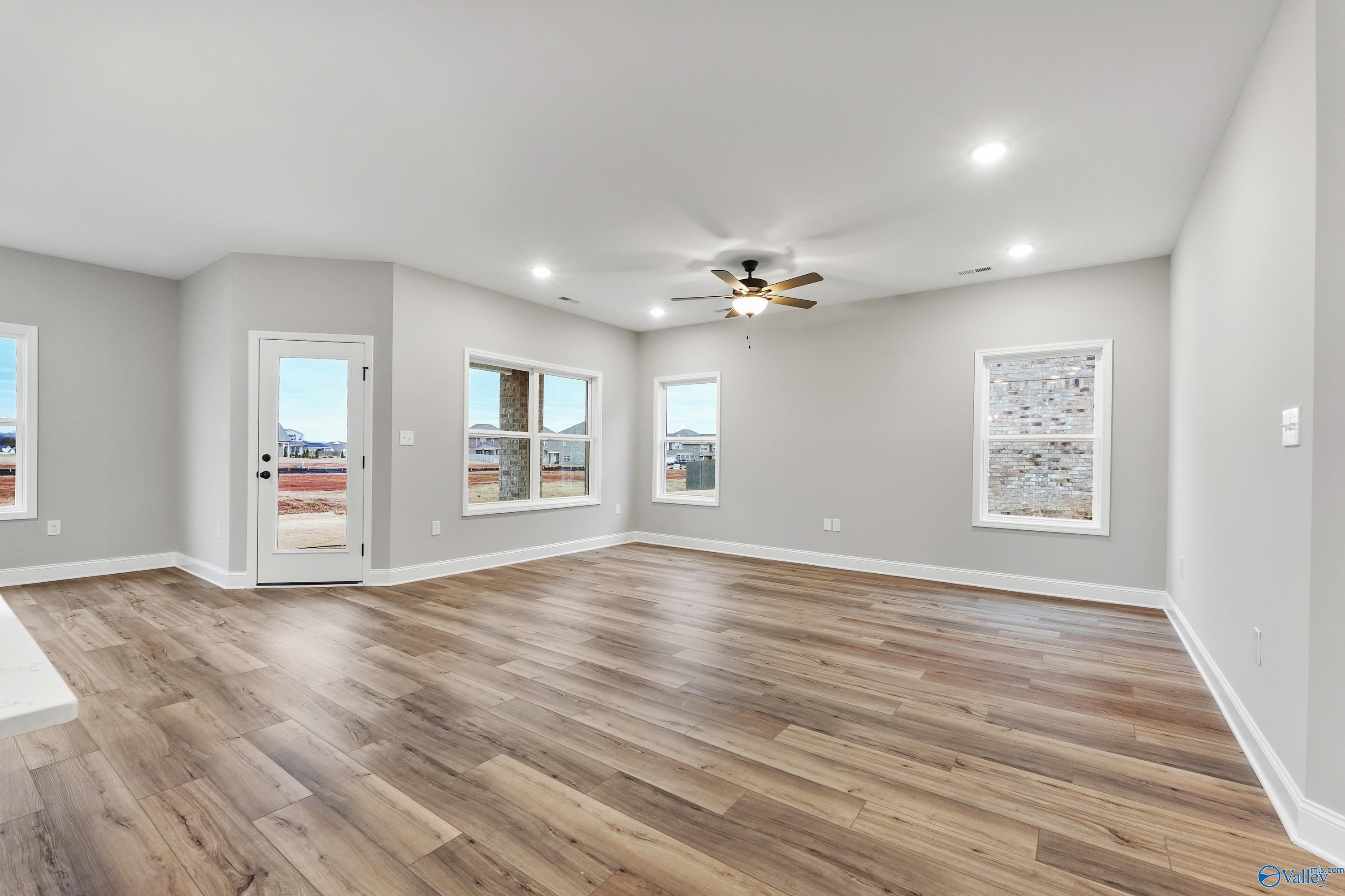 Spacious open living room with gray walls, luxury vinyl plank floors, ceiling fan, and large windows in The Asheville C, Meridianville, AL