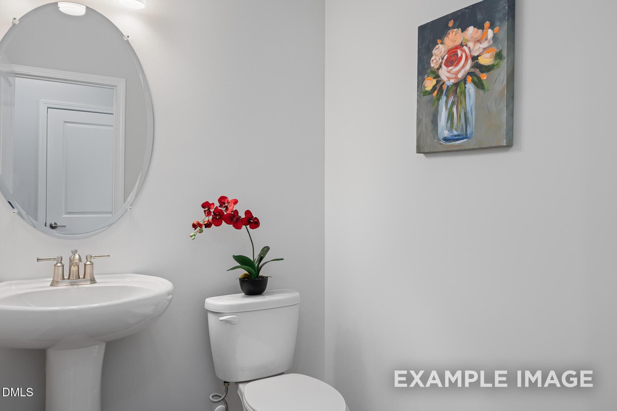Elegant powder room with round mirror, pedestal sink, white toilet, red orchid, floral wall art in Davidson Homes The Cypress B II, Angier, NC