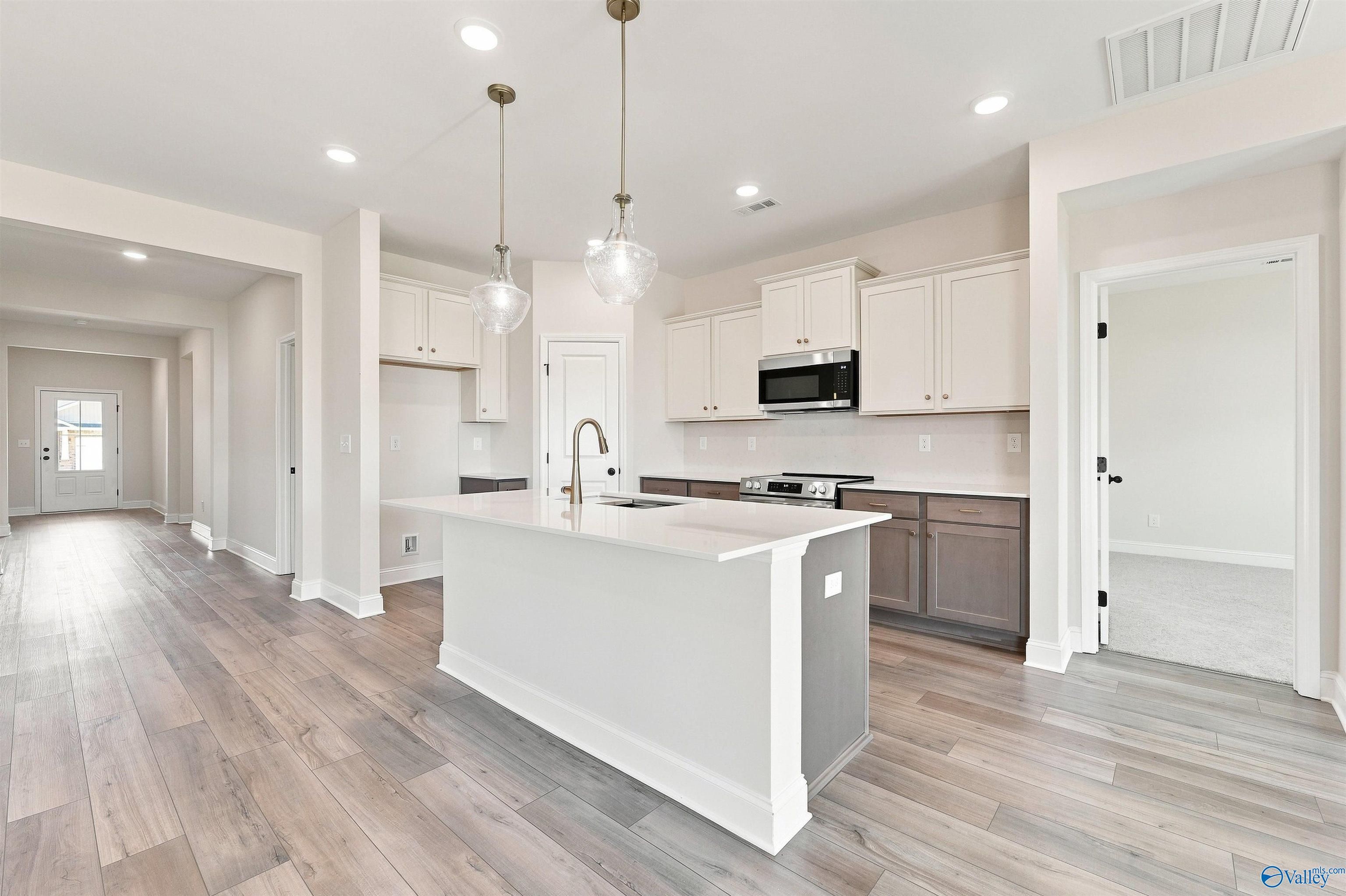 Bright open-concept kitchen with white island, pendant lights, and hardwood floors in The Everett B floor plan, Ivy Hills, Toney, Alabama