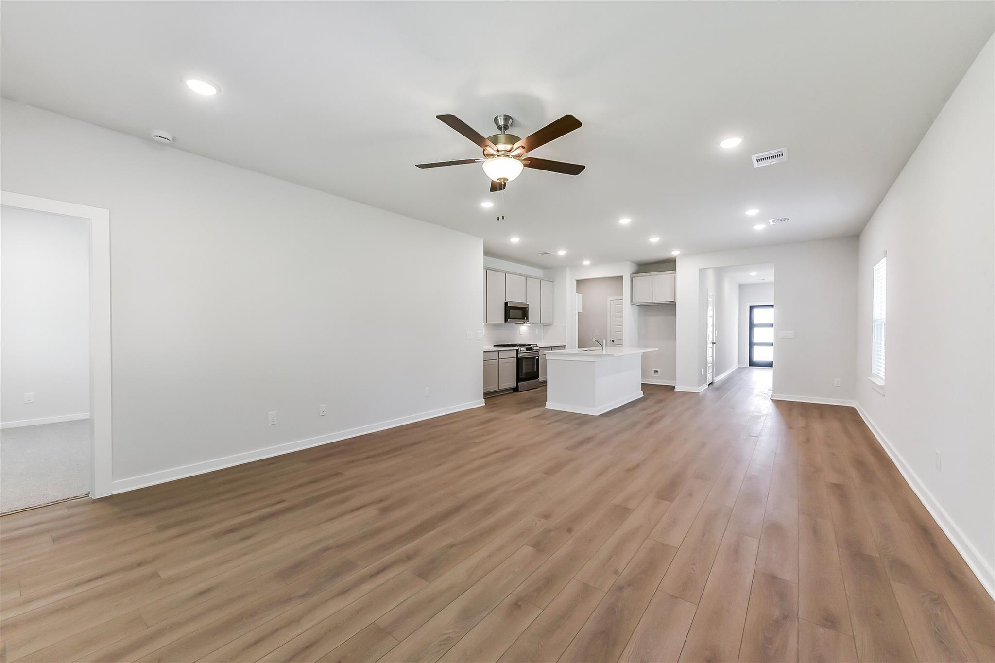 Open-concept living and kitchen with white cabinets, large island, ceiling fan, hardwood floors in The Brazos E by Davidson Homes, Magnolia, TX