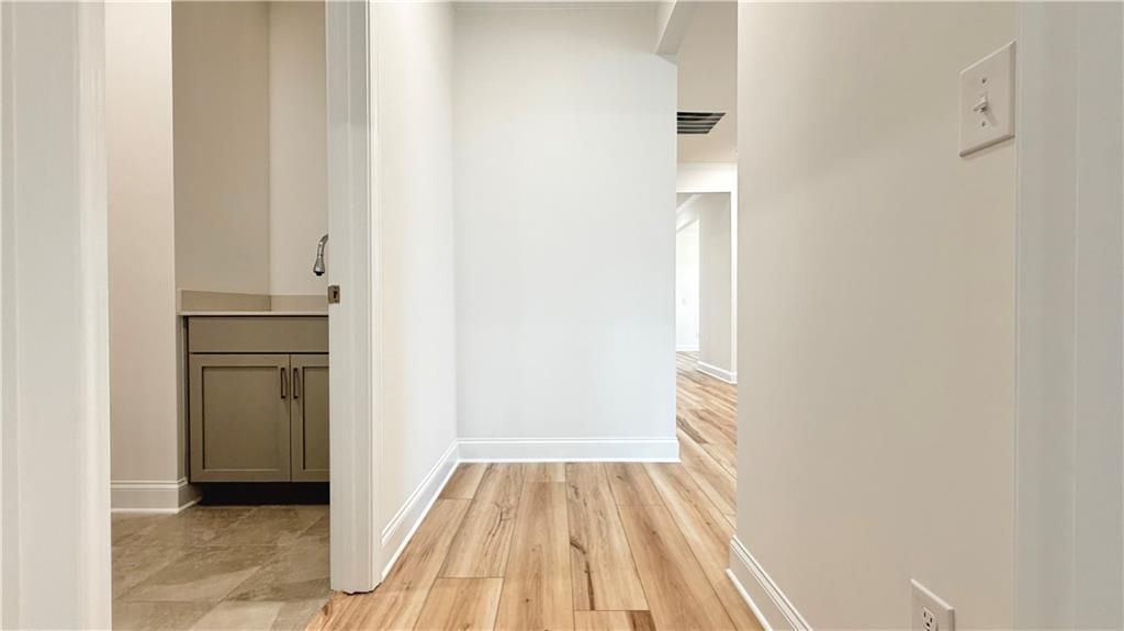 Modern hallway with wood-look flooring leading to a half bath in The Glenwood A floor plan at Wehunt Meadows, Hoschton, GA.