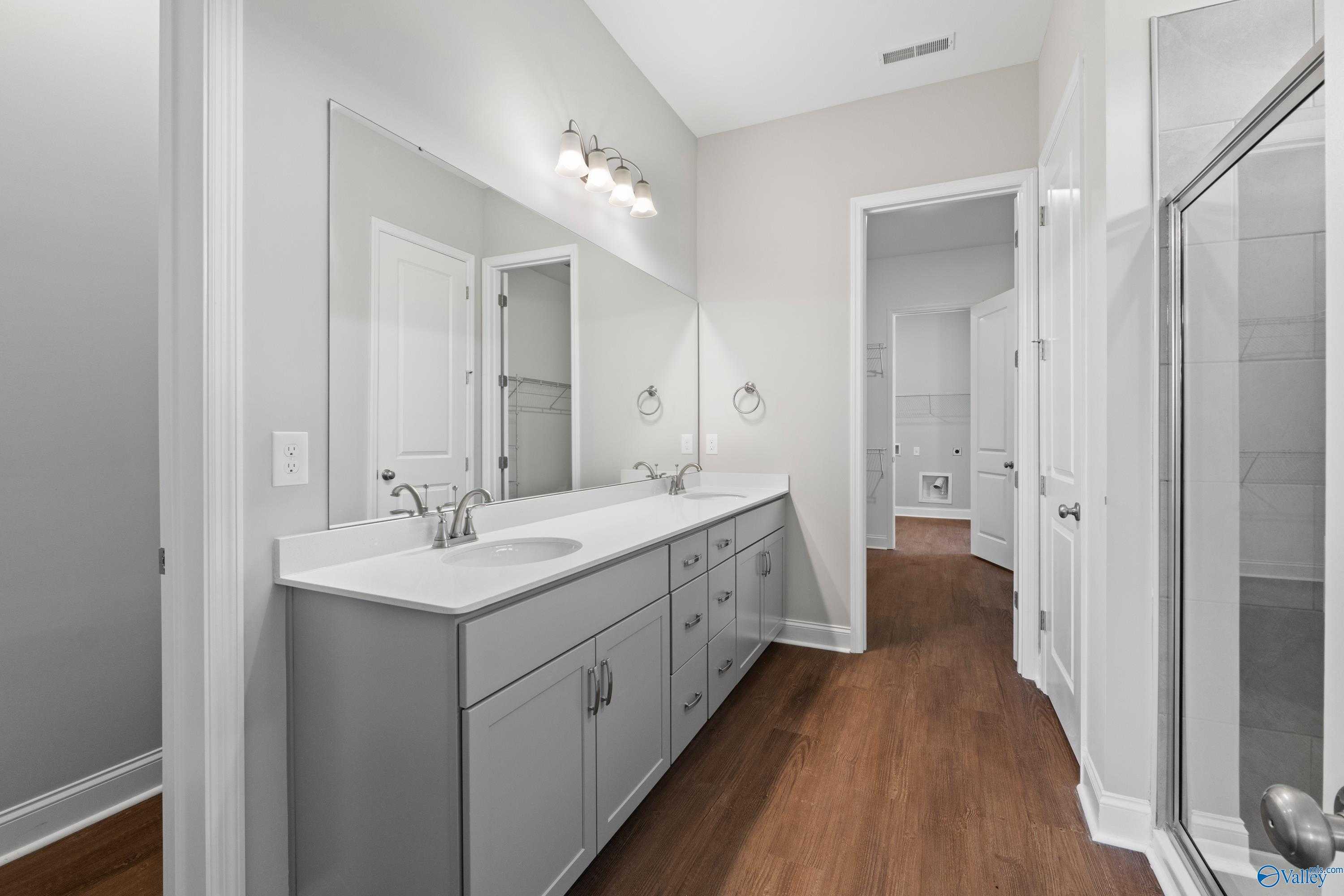 Modern master bathroom featuring double gray vanity, white counters, large mirrors, and glass shower in Davidson Homes The Arcadia, Huntsville, Alabama