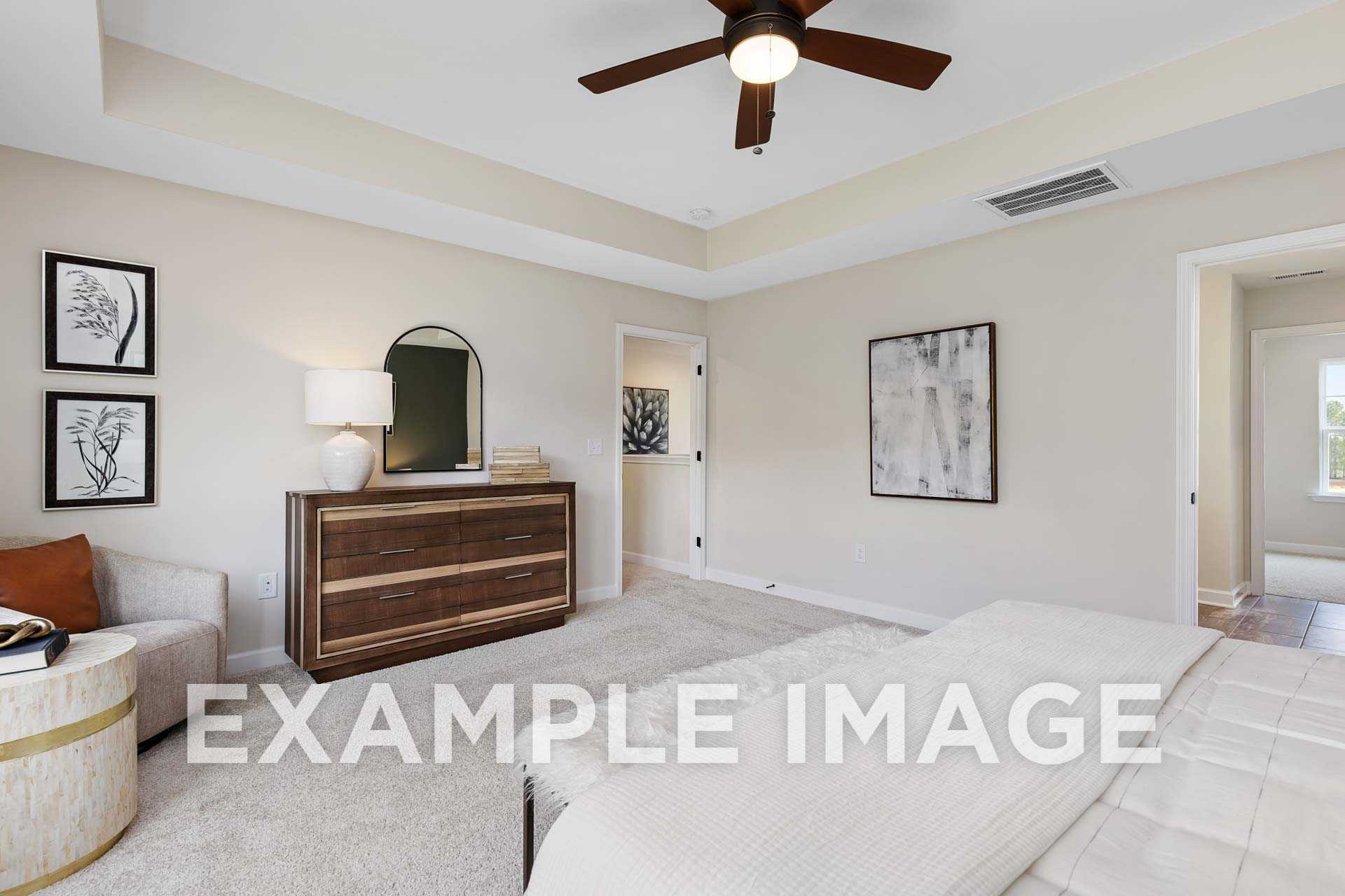 Spacious master bedroom in The Willow F by Davidson Homes, Wake Forest NC, with beige walls, ceiling fan, arched mirror, wooden dresser, and plush white bedding