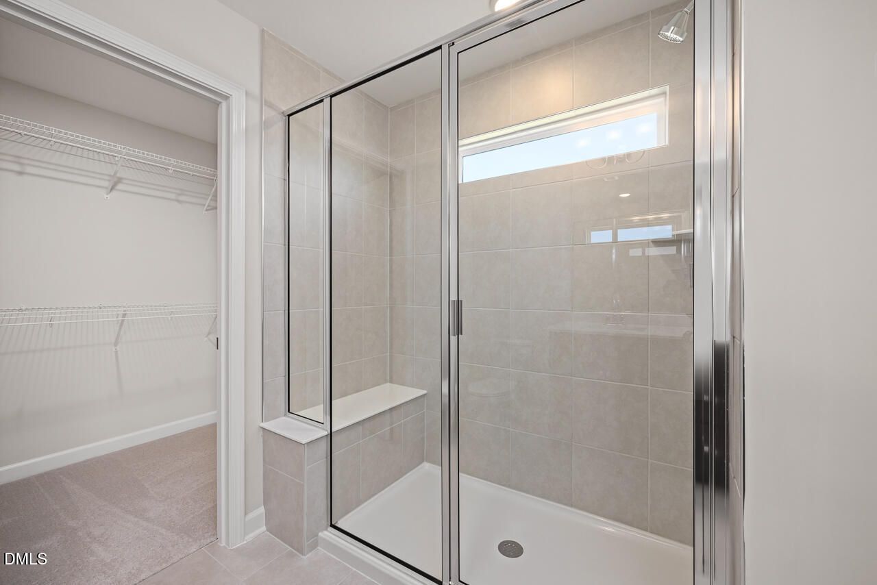 Tiled walk-in shower with bench seat and glass enclosure in The Grace C floor plan at Retreat at North Main, Lillington.