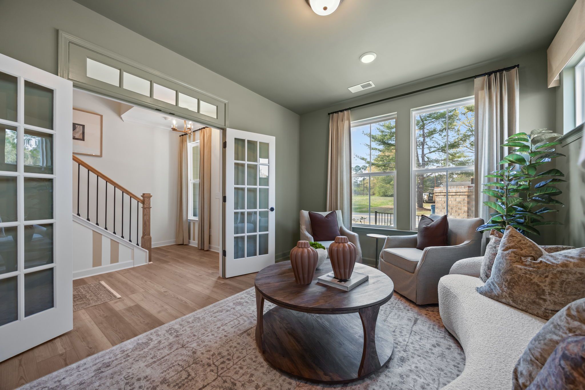 Cozy living room at Camden Park in Knightdale NC with curved white sofa, accent chairs, French doors, hardwood floors, and large windows