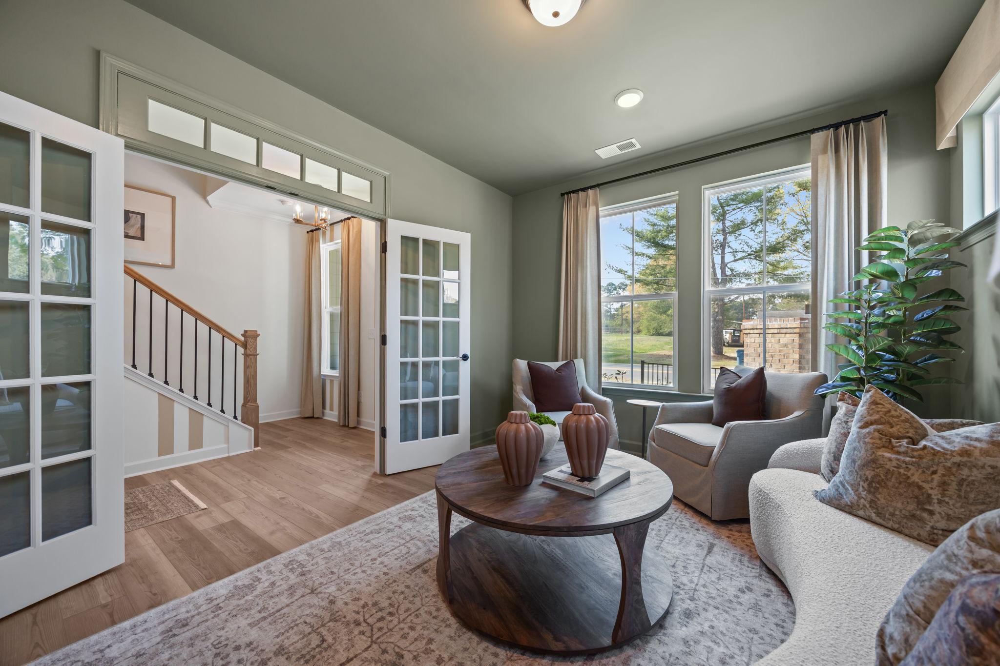Cozy living room at Camden Park in Knightdale NC with curved white sofa, accent chairs, French doors, hardwood floors, and large windows